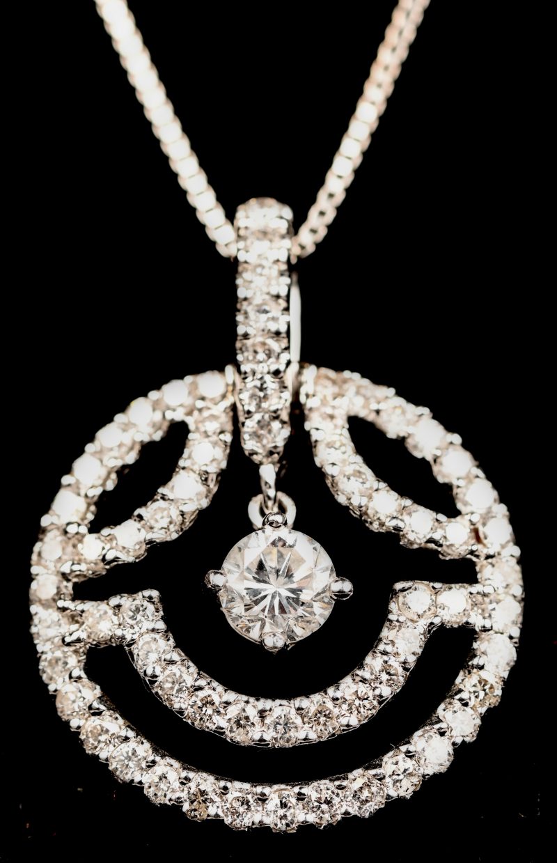 Een 18 kt witgouden ketting met hanger met een centrale briljant 0,26 ct, en briljanten met een gezamenlijk gewicht van 0,58 ct.