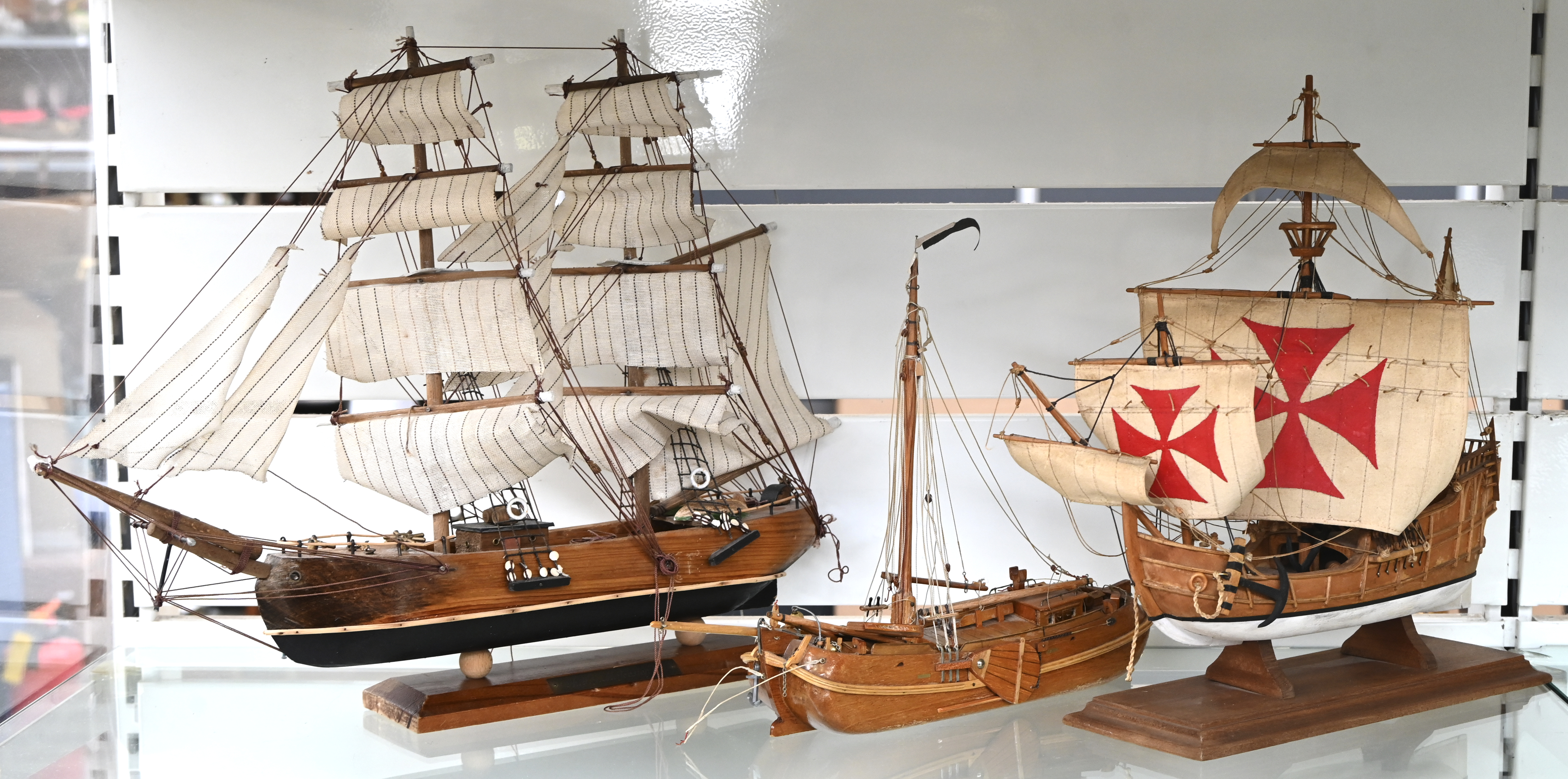 Drie diverse houten scheepsmaquettes. Een kleine platbodem, de Santa Maria en een driemaster Drie diverse houten scheepsmaquettes. Een kleine platbodem, de Santa Maria en een driemaster.