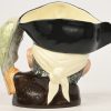 Een gekleurde creamware “character jug” in de vorm van het hoofd van Long John Silver met zijn papegaai. Onderaan gemerkt.