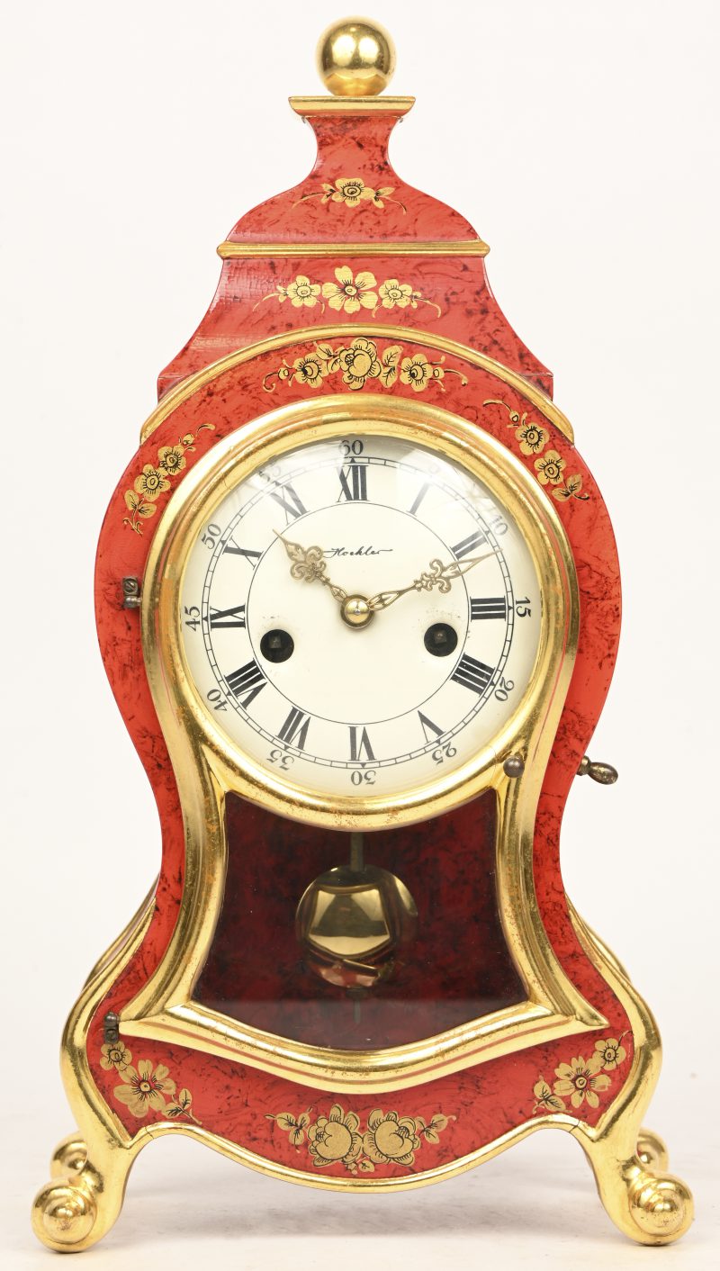 Een kleine pendule, rood en goud gelakt in de stijl van Neuchatel. Met slinger en sleutel.