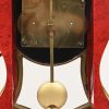 Een kleine pendule, rood en goud gelakt in de stijl van Neuchatel. Met slinger en sleutel.