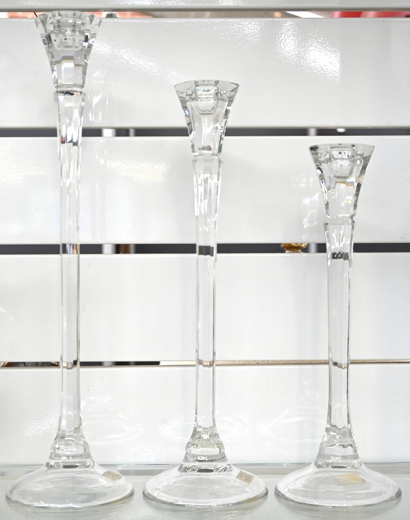 Drie lange kandelaars van kleurloos glas, in lengte afnemend.