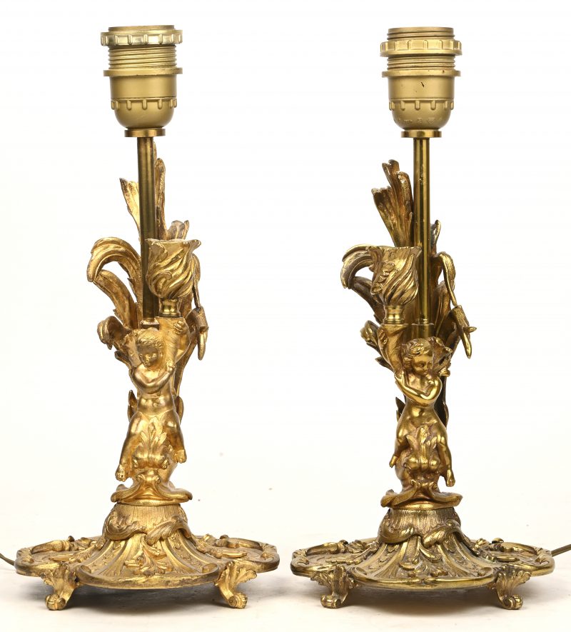 Een paar vergulde bronzen kandelaars, vegetaal van vorm en gedragen door putti. Op elektriciteit.