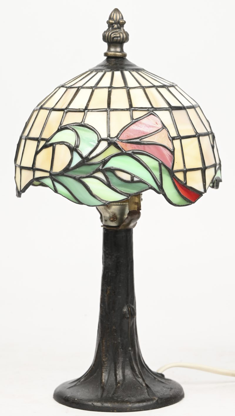 Een kleine schemerlamp met een bronzen voet en een glas-in-lood kap in e geest van Tiffany.