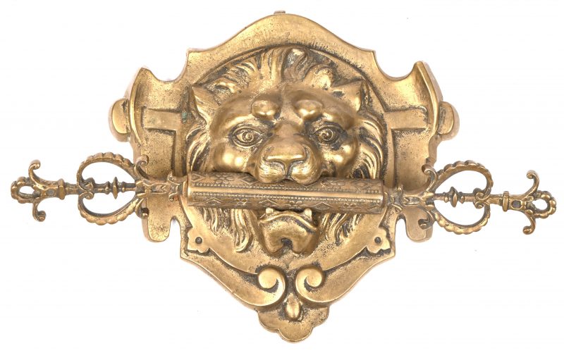 Een bronzen leeuwenkop met een dubbele sleutel in de bek. Mogelijk als meubelversiering. Omstreeks 1900.