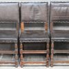 Een reeks van zes eikenhouten stoelen met lederen bekleding met klinknagels.