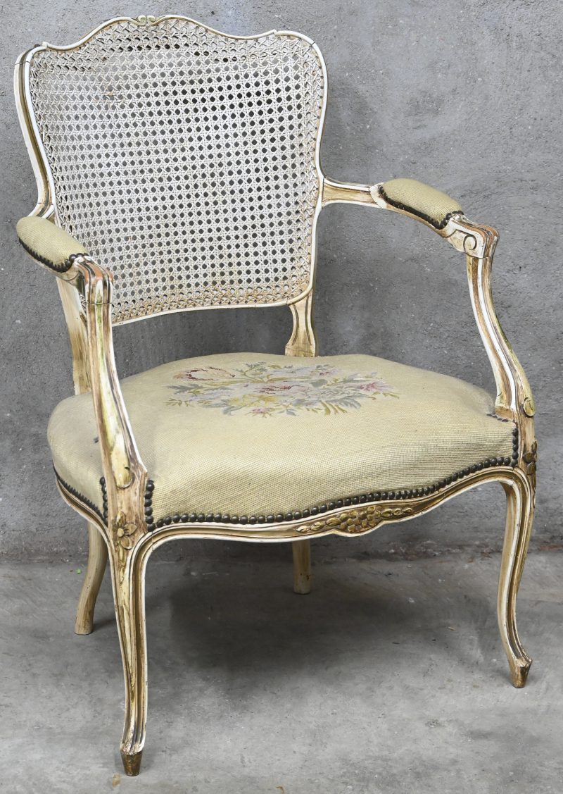 Een gepatinneerde houten armstoel in Lodewijk XV-stijl. Met cannage rugleuning, zitting versierd met naaldwerk “petit point”.