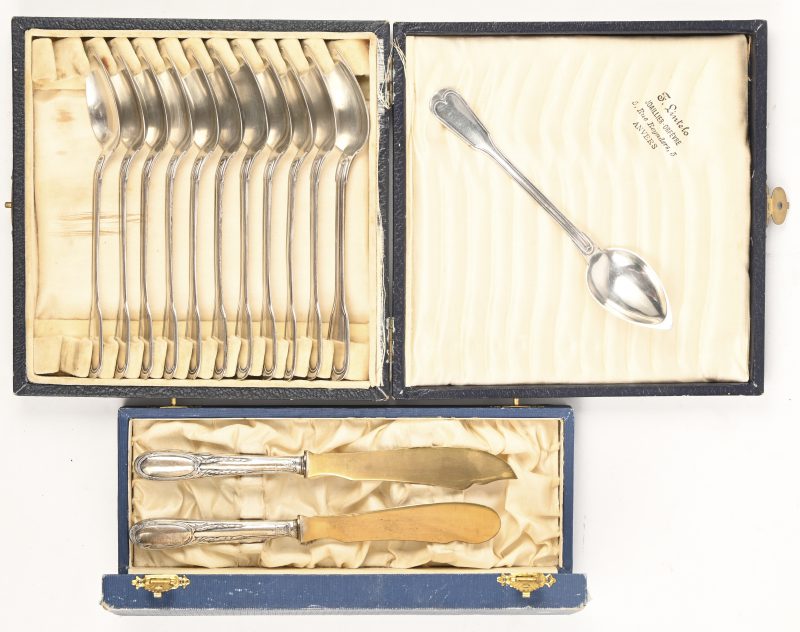 Een set van 12 zilveren lepeltjes in casette, met een bruto gewicht van 265 gram. Gemerkt; Delheid. Toegevoegd twee mesjes met een zilveren heft, gemerkt; 800.
