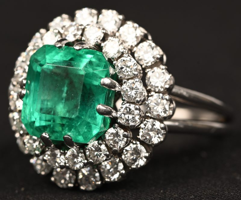 Een platina ring bezet met een centrale smaragd van +- 5,15 ct. en diamanten met een gezamenlijk gewicht van +- 1,60 ct.