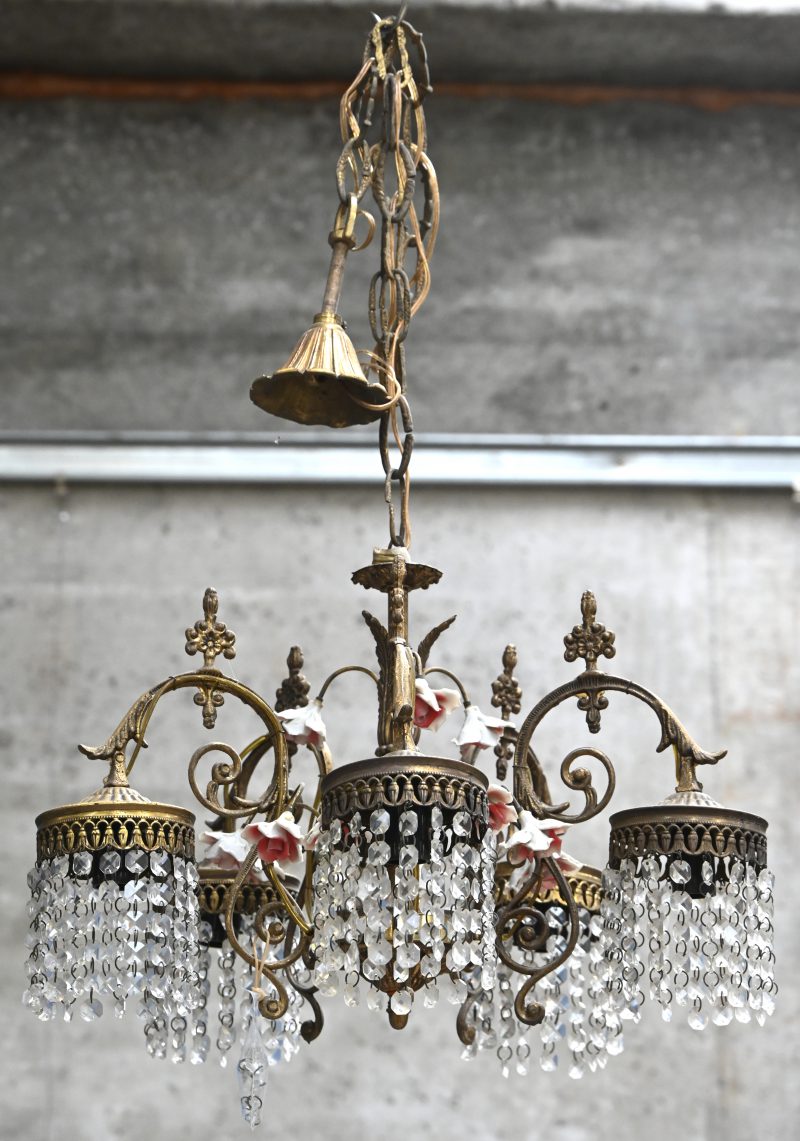 Een koperen hanglamp met kristallen en porseleinen bloemetjes.