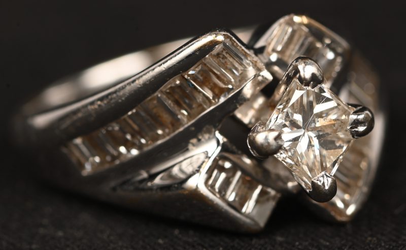 Een 14 kt witgouden ring bezet met een centrale diamant in princess geslepen van +- 0,50 ct.  en baguettes met een gezamenlijk gewicht van +- 1 ct.