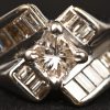 Een 14 kt witgouden ring bezet met een centrale diamant in princess geslepen van +- 0,50 ct.  en baguettes met een gezamenlijk gewicht van +- 1 ct.