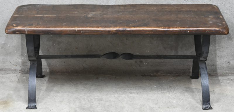 Een rustieke salontafel, massief houten blad en smeedijzeren onderstel.