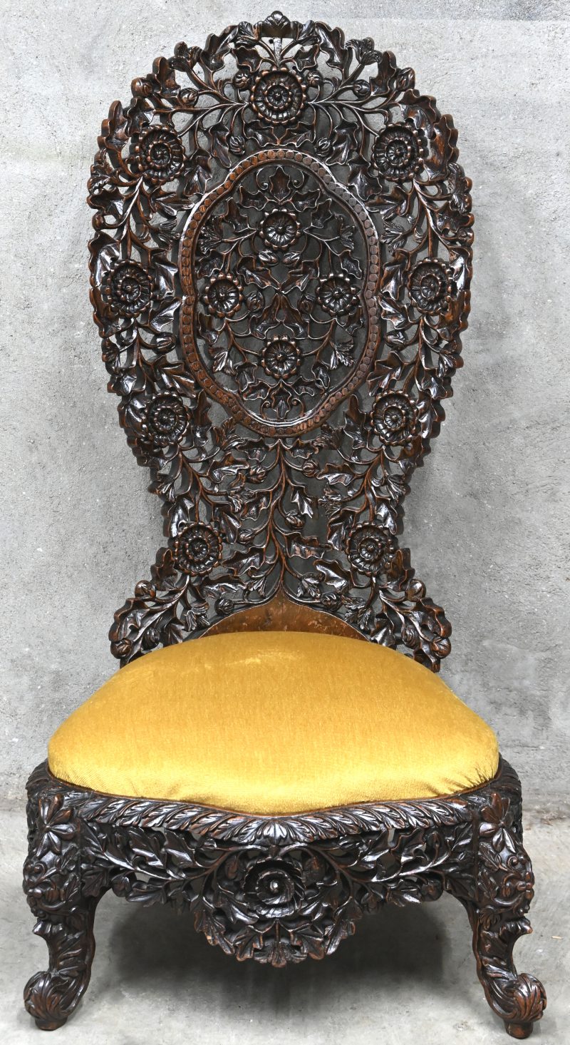Een rijkelijk gesculpteerde houten sierstoel, met een lage zit en een hoge rug.