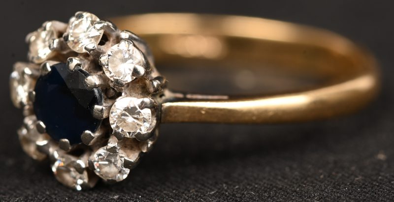 Een 18 kt wit- en geelgouden ring bezet met een centrale saffier van +- 0,40 ct. en briljanten met een gezamenlijk gewicht van +- 0,40 ct.