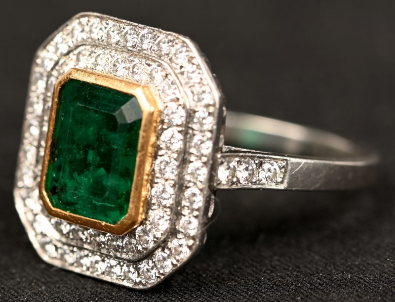 Een 18 kt wit- en geelgouden ring bezet met een centrale Columbiaanse smaragd gewicht van +- 2 ct. en met briljanten met een gezamenlijk gewicht van +- 0,60 ct.