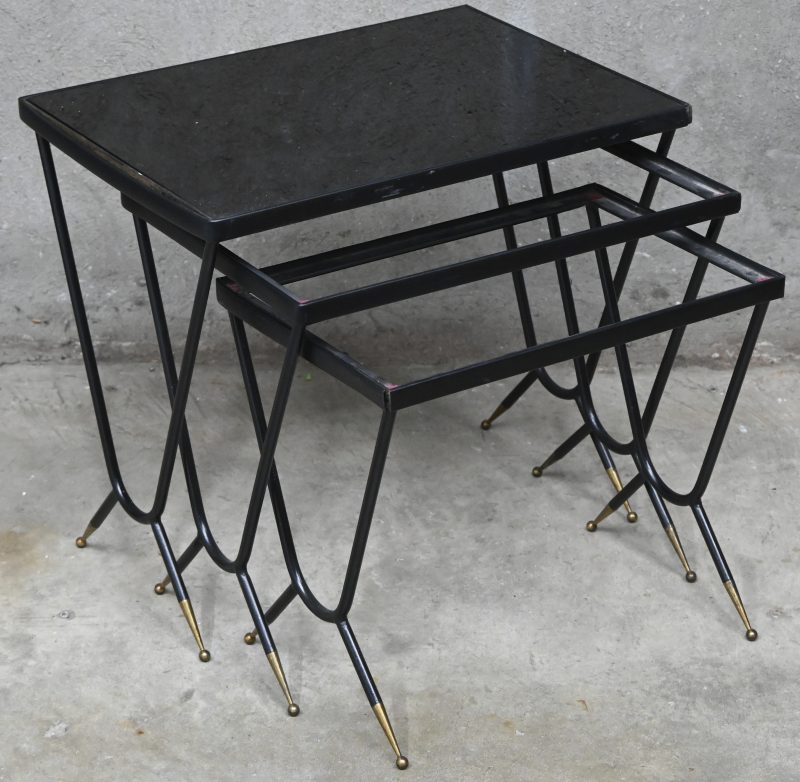 Een set van 3 midcentury nesting tables, gelakt staal en messing pootjes, het grootste heeft nog zijn fumé glazen blad, dit is manco bij de kleinste tafeltjes.