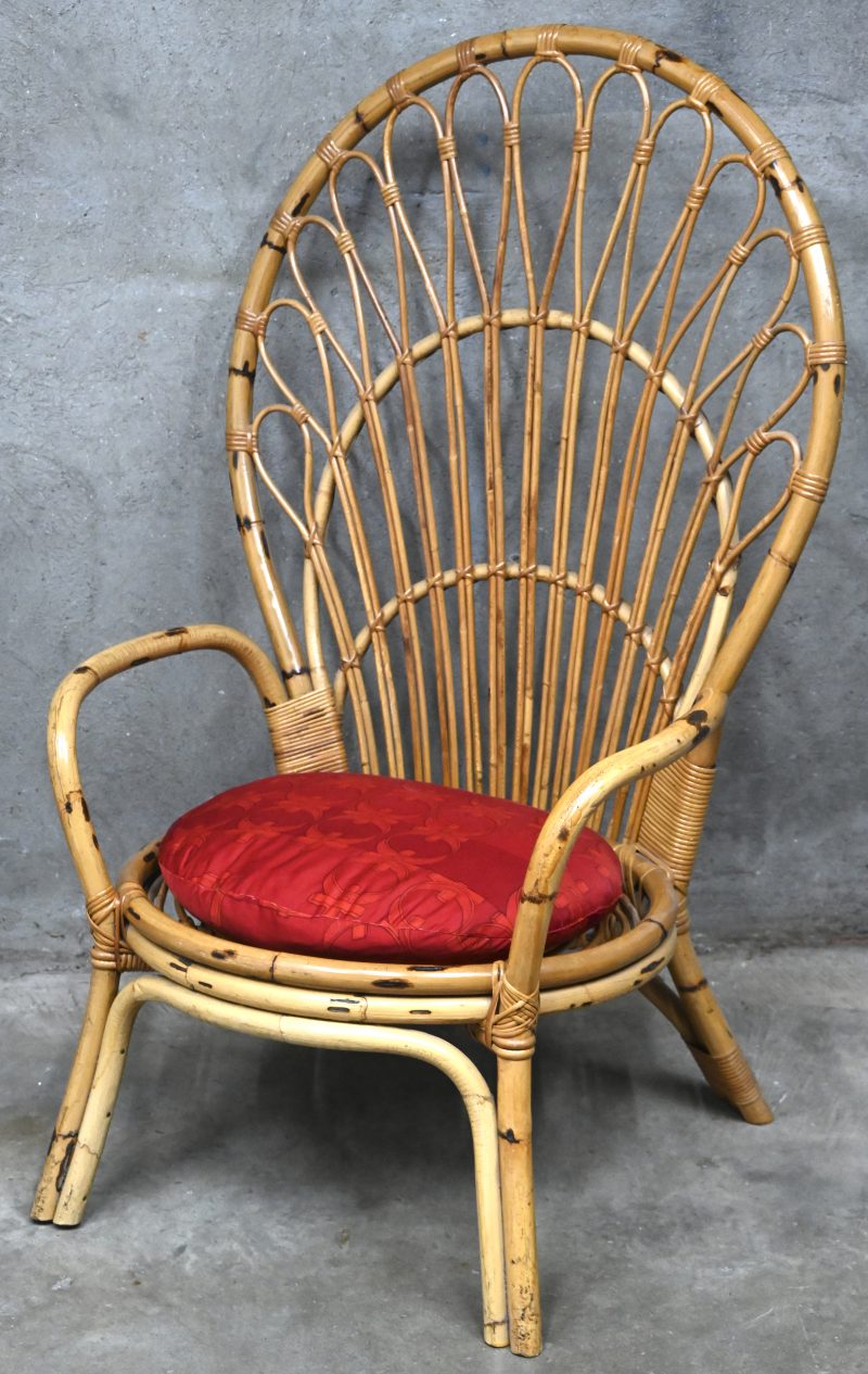 Een vintage rotan pauwenstoel met rood stoffen zitkussen.