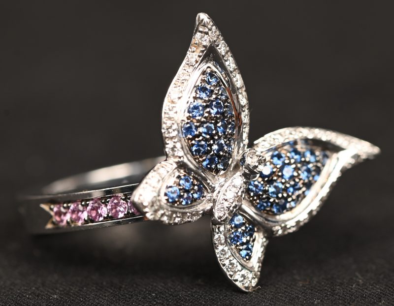 Een 18 kt witgouden in de vorm van een vlinder bezet met briljanten, roze en blauwe saffieren met een gezamenlijk gewicht van +- 1 ct. In originele doos.