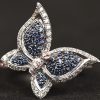 Een 18 kt witgouden in de vorm van een vlinder bezet met briljanten, roze en blauwe saffieren met een gezamenlijk gewicht van +- 1 ct. In originele doos.