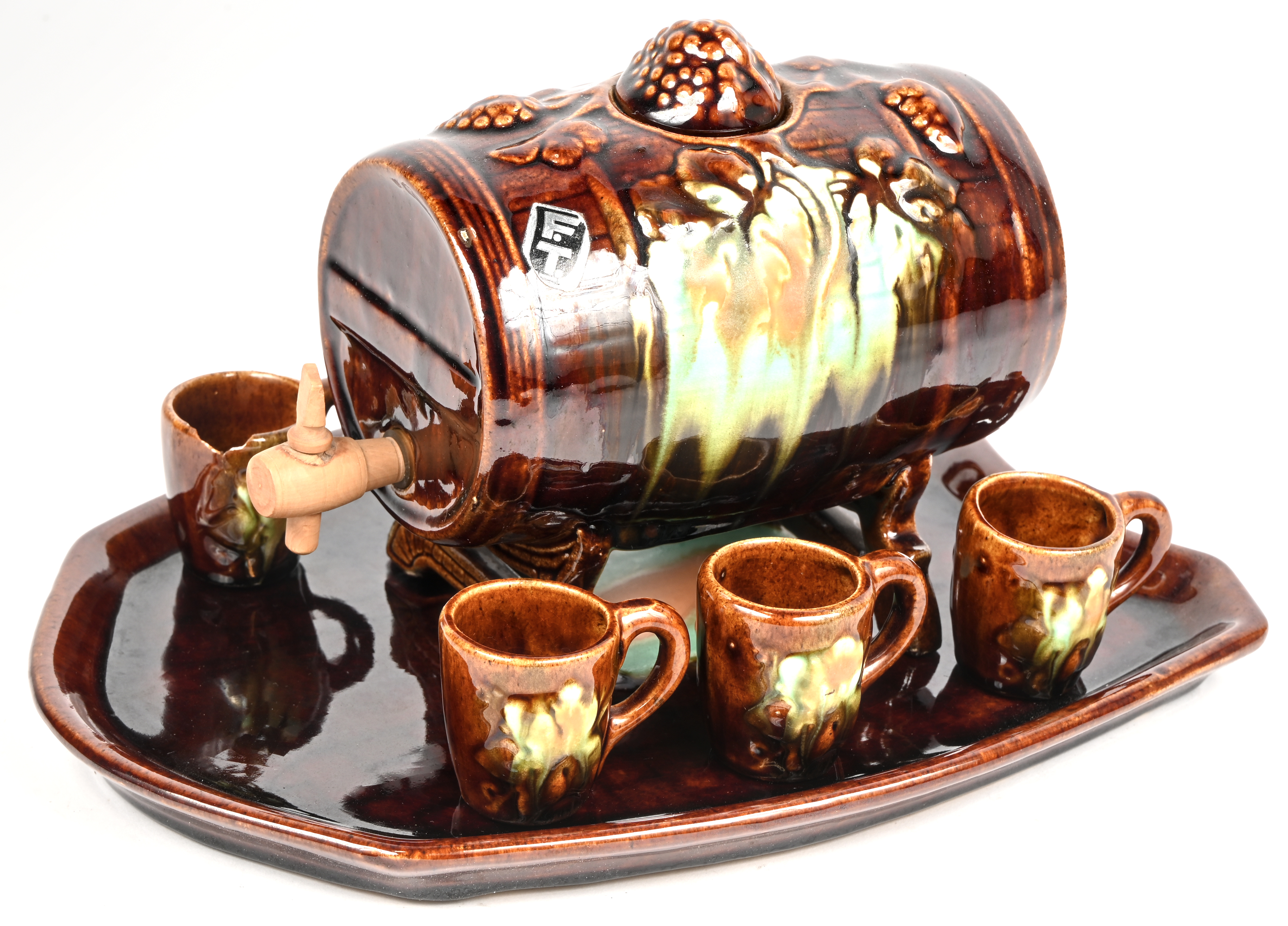 Een druiventonnetje met onderschaal en likeurset in Vlaams aardewerk. ‘Belgium 126’. Met zes ‘glaasjes’ waarvan één gebroken Een druiventonnetje met onderschaal en likeurset in Vlaams aardewerk. ‘Belgium 126’. Met zes ‘glaasjes’ waarvan één gebroken.