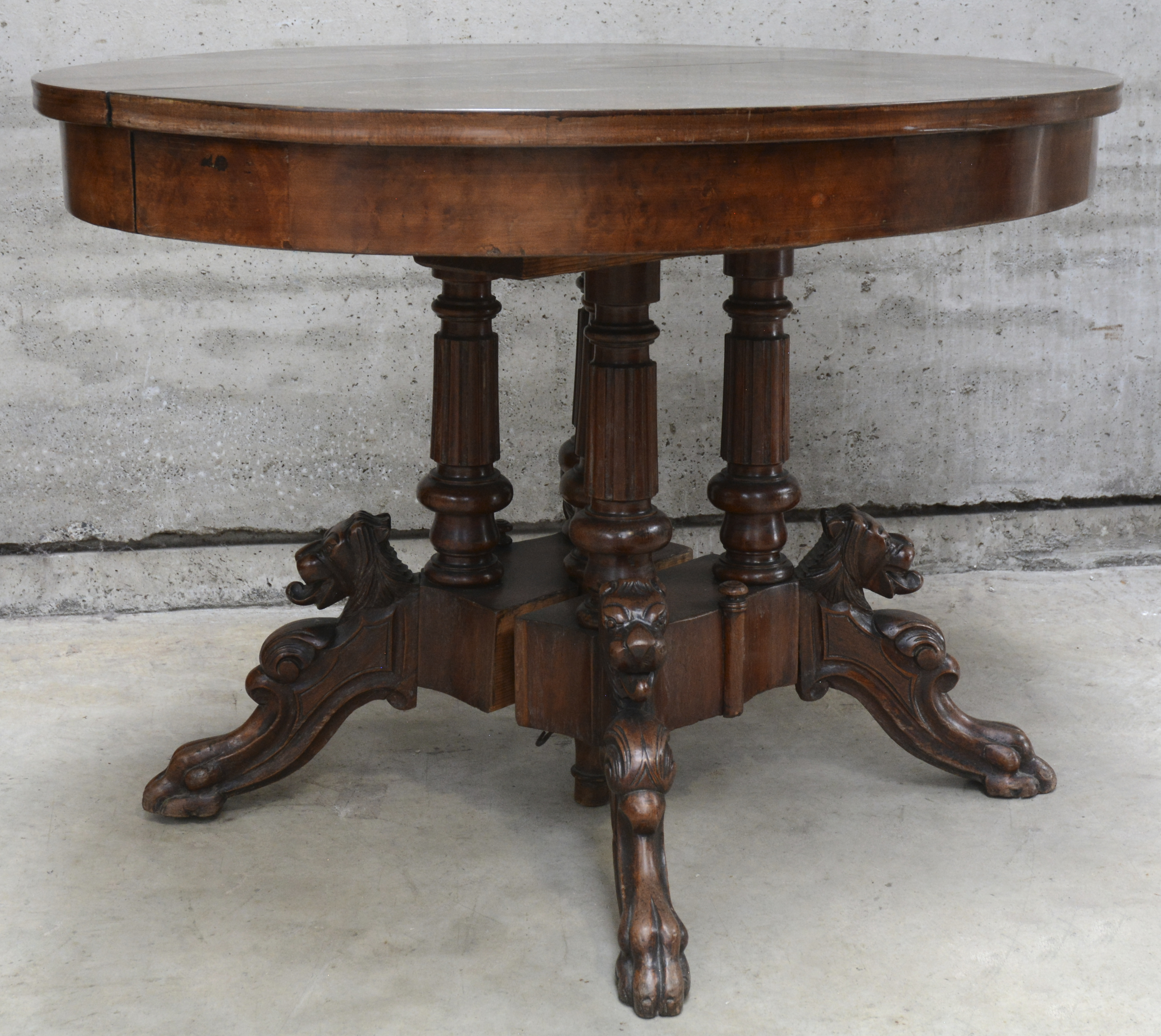 Een verlengbare ronde eetkamertafel met een centrale vierpoot versierd met vossenkoppen Een verlengbare ronde eetkamertafel met een centrale vierpoot versierd met vossenkoppen.