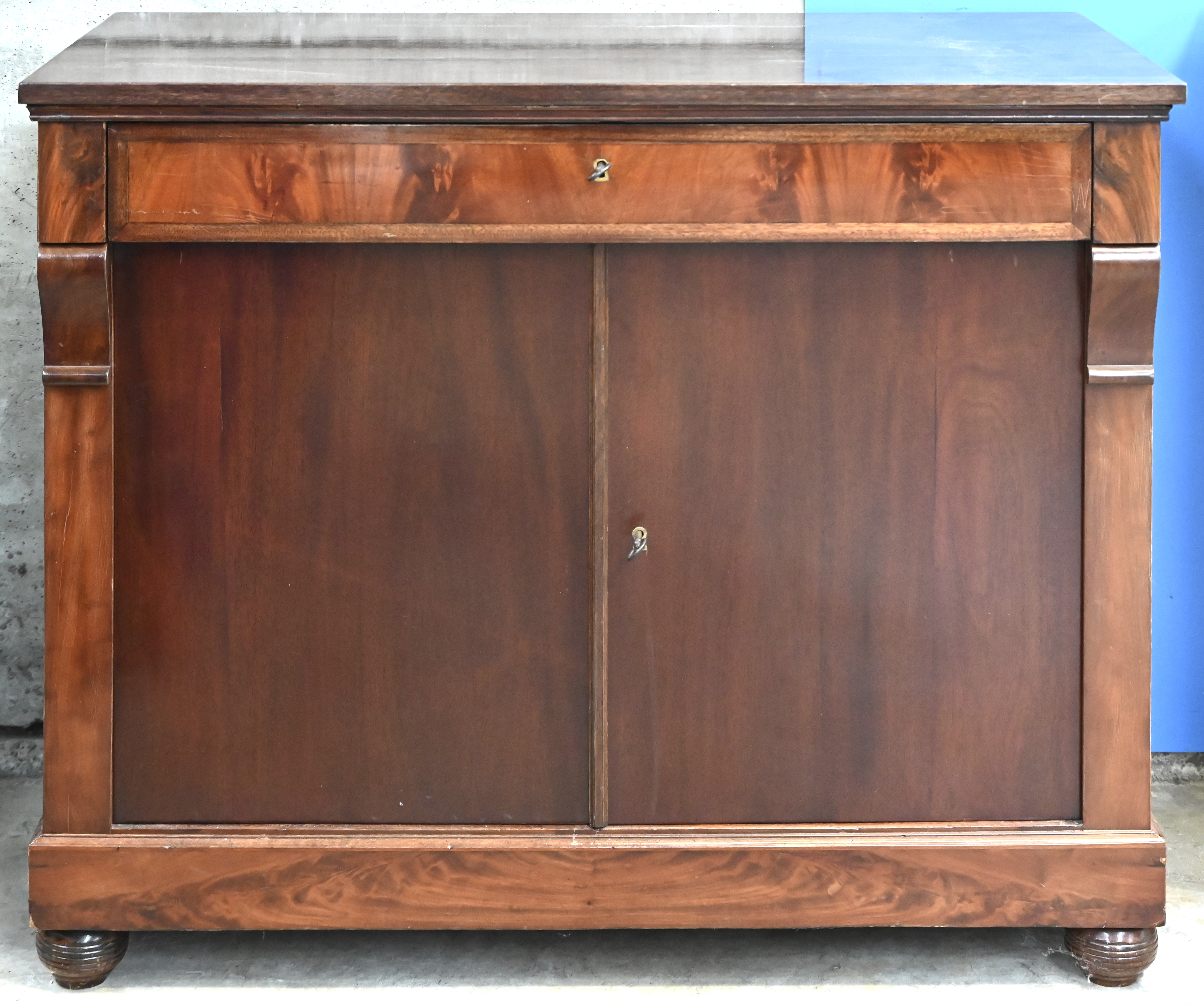 Een massief houten commode met gefineerde fronten. 2 deuren en 1 lade voorzien voor bestek Een massief houten commode met gefineerde fronten. 2 deuren en 1 lade voorzien voor bestek.