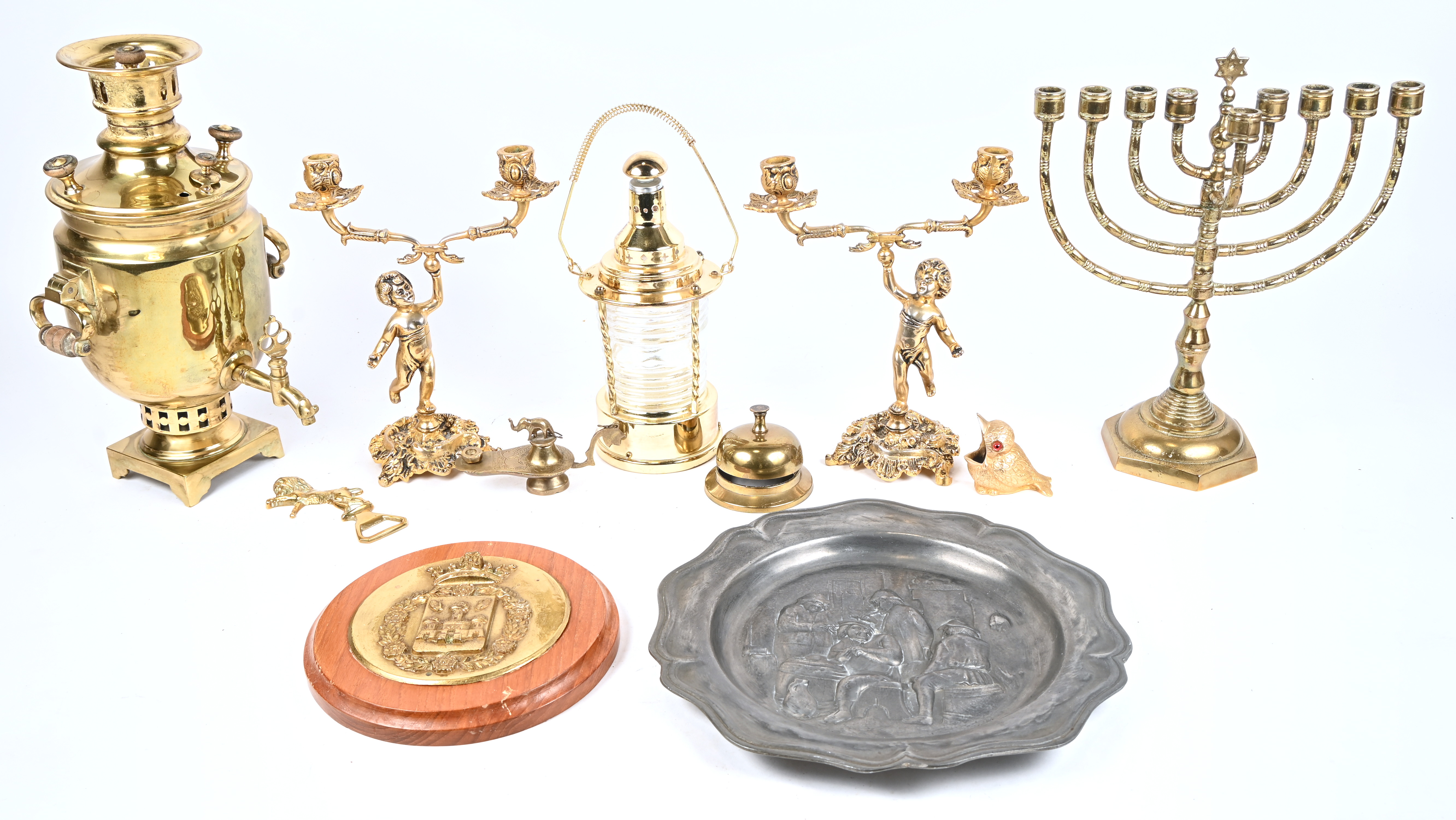 Een lot bestaande uit messng: een paar kandelaars gedragen door engeltjes, een menorah, een kleine scheepslamp, een samovar, een toogbel, een vegeltje, een plaquette van Antwerpen, een olielamp, een flessenopener met heraldische leeuw. Evenals een tinnen schotel en een zakmes Een lot bestaande uit messng: een paar kandelaars gedragen door engeltjes, een menorah, een kleine scheepslamp, een samovar, een toogbel, een vegeltje, een plaquette van Antwerpen, een olielamp, een flessenopener met heraldische leeuw. Evenals een tinnen schotel en een zakmes.