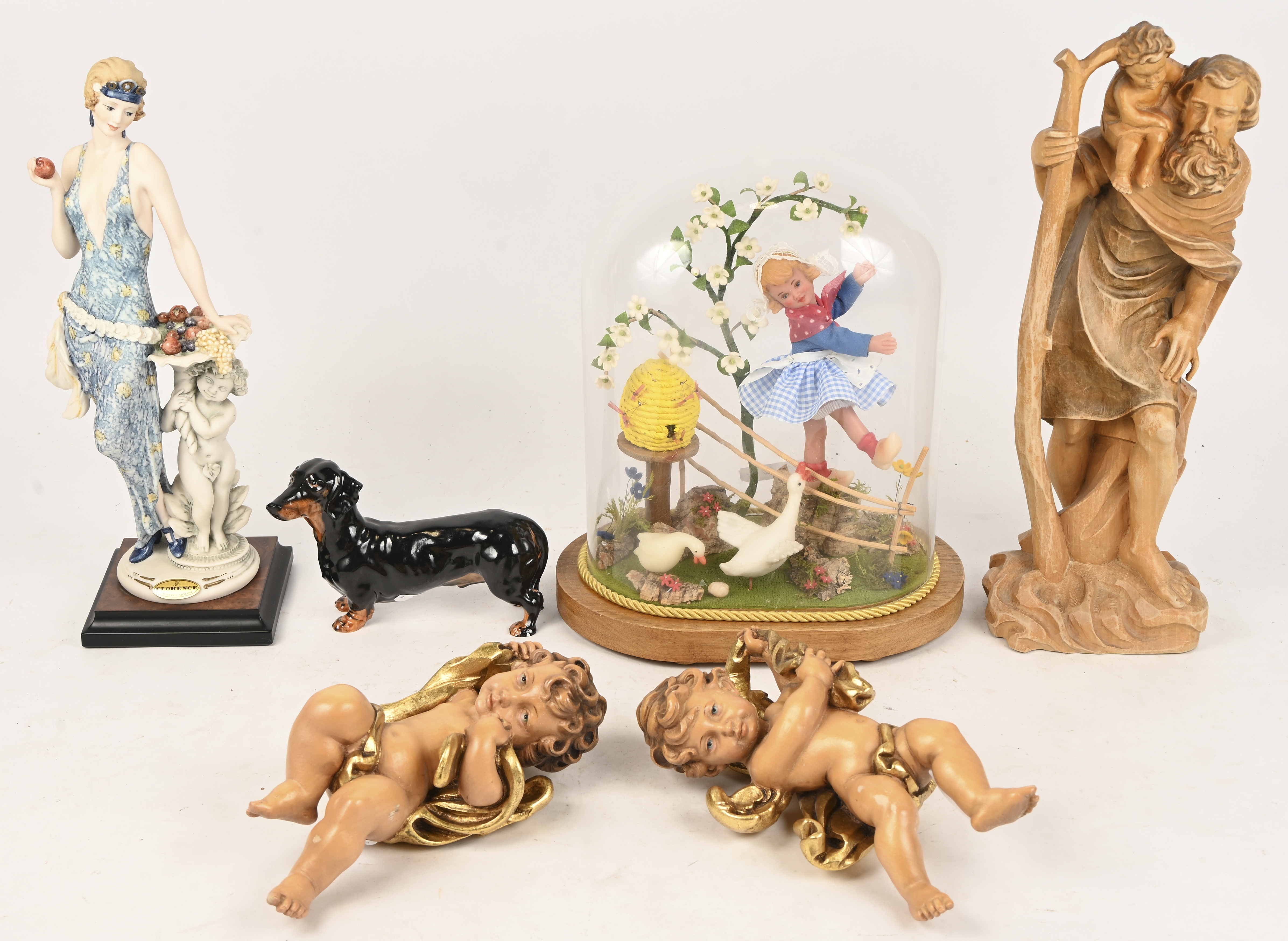 Een gevarieerd lot met een houten St-Christoffel, twee barokke engeltjes, een porseleinen teckel, een kunststof beeldje van een jonge vrouw en een stolp met een compositie door de Arme Klaren Een gevarieerd lot met een houten St-Christoffel, twee barokke engeltjes, een porseleinen teckel, een kunststof beeldje van een jonge vrouw en een stolp met een compositie door de Arme Klaren.