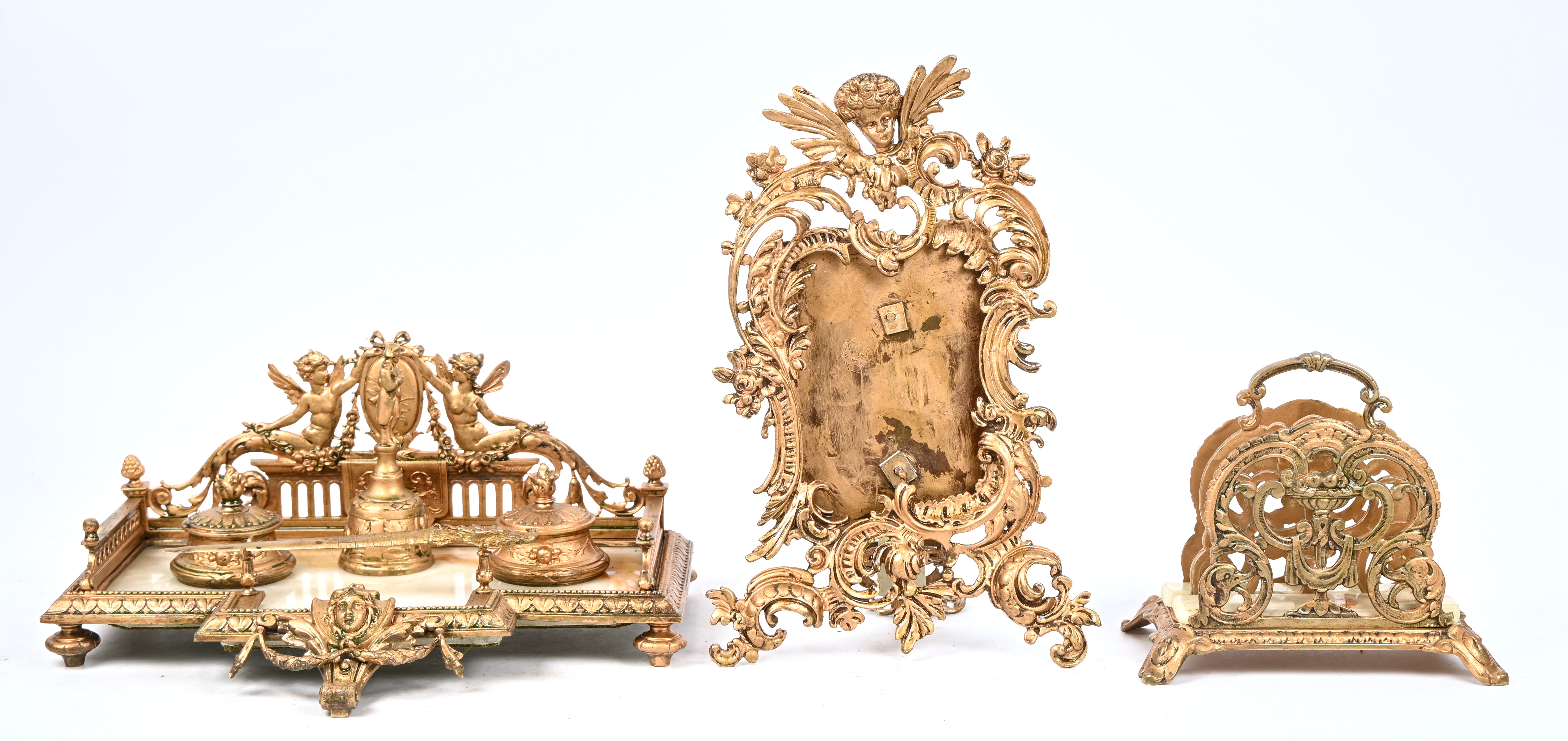 Een bureaugarnituur van goudkleurig metaal en onyx. Bestaande uit een inkstel versierd met een Napoleonbeeldje, een paar penhouders, een paar kandelaars, een paar cassolettes, een brievenhouder, een briefopener, een schemerlamp, een fotolijst. Directoire stijl, medio XXste eeuw Een bureaugarnituur van goudkleurig metaal en onyx. Bestaande uit een inkstel versierd met een Napoleonbeeldje, een paar penhouders, een paar kandelaars, een paar cassolettes, een brievenhouder, een briefopener, een schemerlamp, een fotolijst. Directoire stijl, medio XXste eeuw.