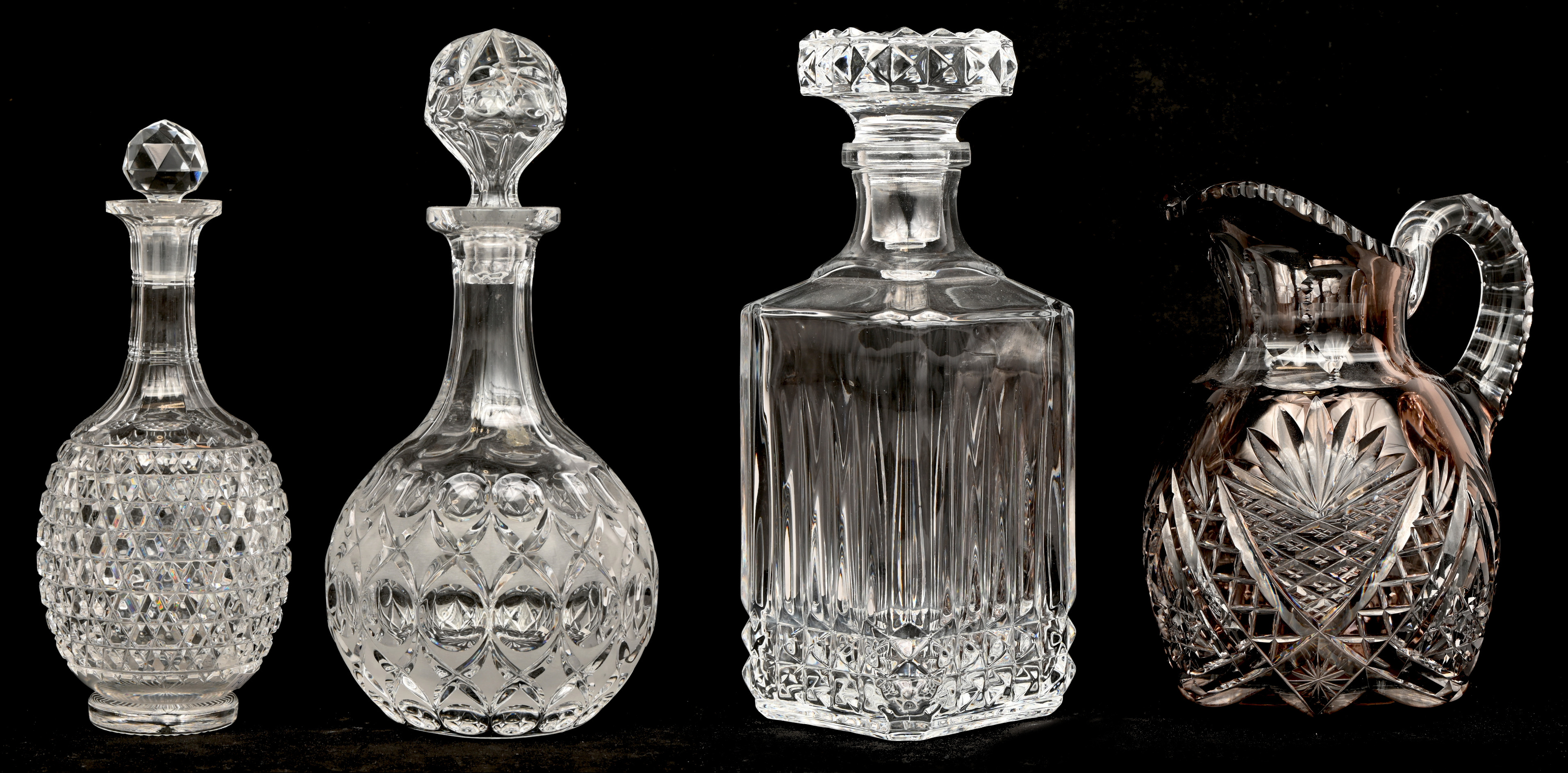 Een gevarieerd lot kleurloos en gekleurd kristal bestaande uit drie karaffen en een schenkkan Een gevarieerd lot kleurloos en gekleurd kristal bestaande uit drie karaffen en een schenkkan.