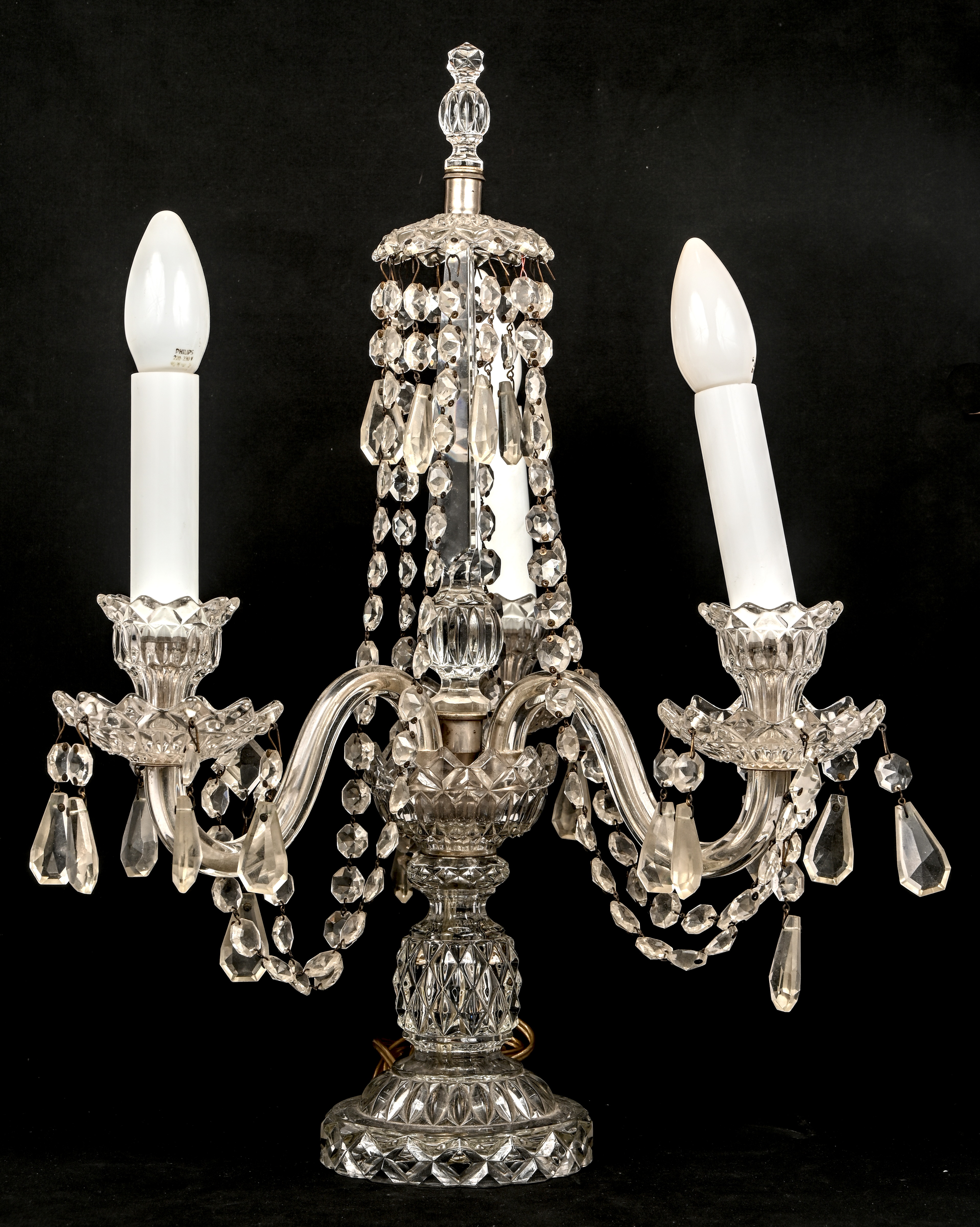 Een tafellamp gevormd als een kandelaar met drie armen. Van geperst glas, schade aan 1 van de opaline ‘kaarsen’ Een tafellamp gevormd als een kandelaar met drie armen. Van geperst glas, schade aan 1 van de opaline ‘kaarsen’.