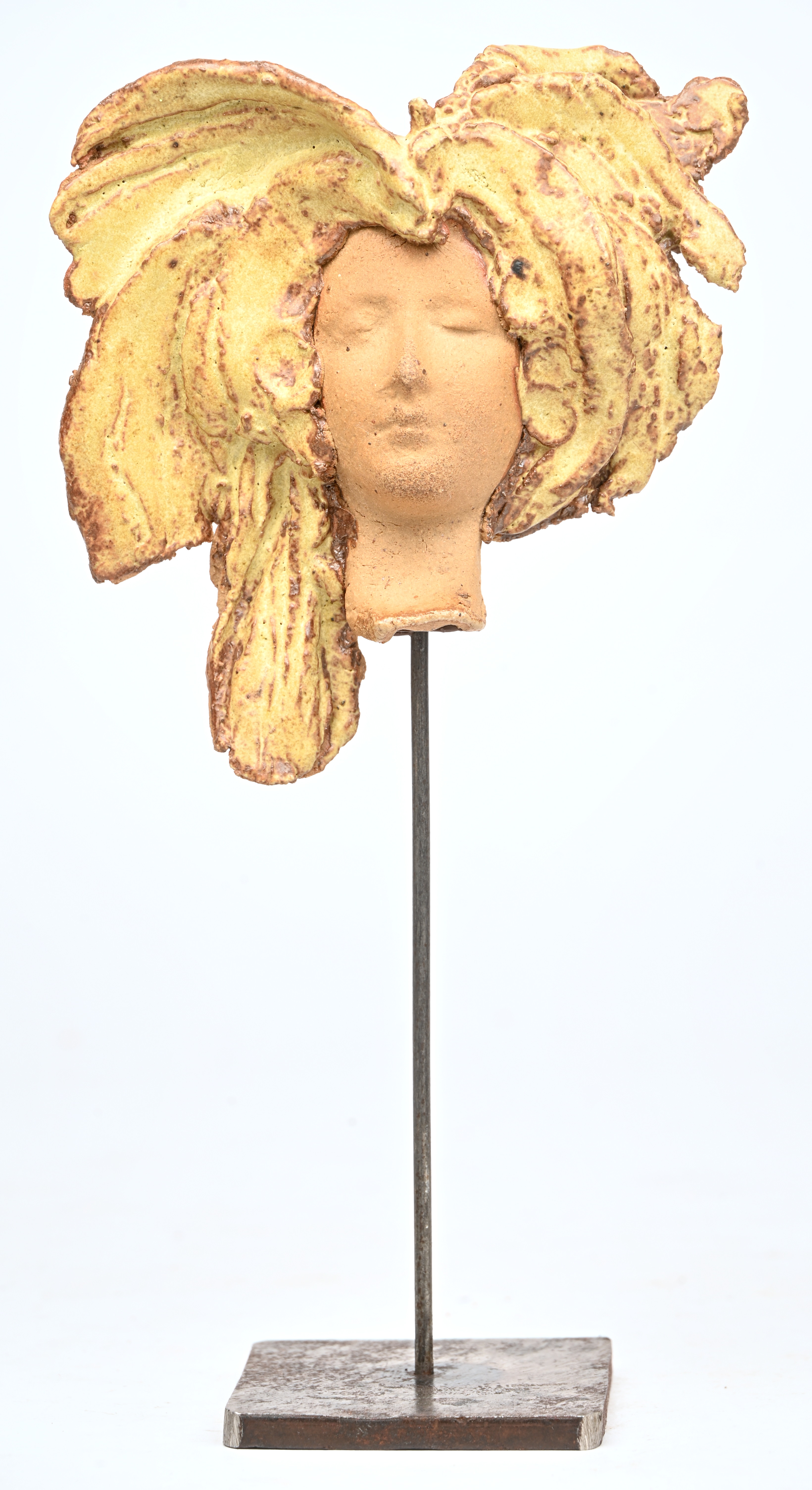 ‘Vrouwenportret met pluimentooi’, een geglazuurd aardewerken beeldje op metalen voet ‘Vrouwenportret met pluimentooi’, een geglazuurd aardewerken beeldje op metalen voet.