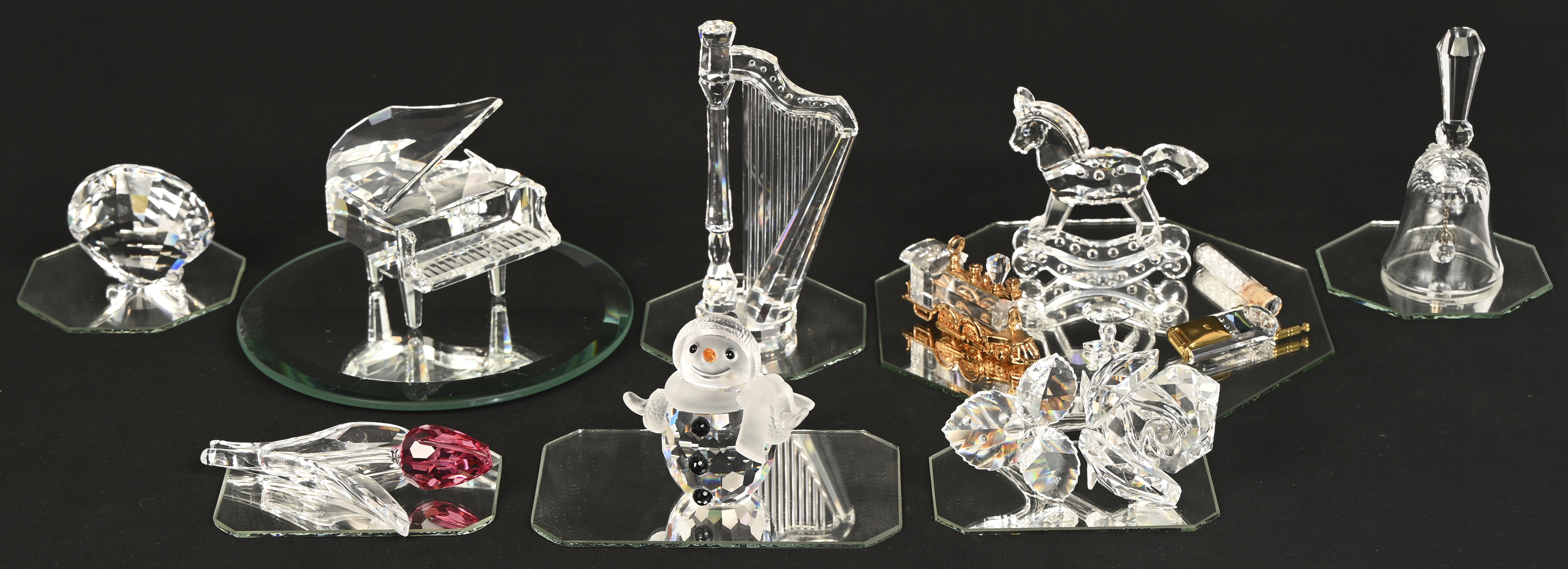 Een lot beeldjes van Swarovski kristal Een lot beeldjes van Swarovski kristal. Bestaande uit; een piano, een trein, een mobiele telefoon, een vleugelpiano, twee bloemen, een schommelpaard, een schelp, een belletje, een sneeuwman, een tafeltje en een buisje met