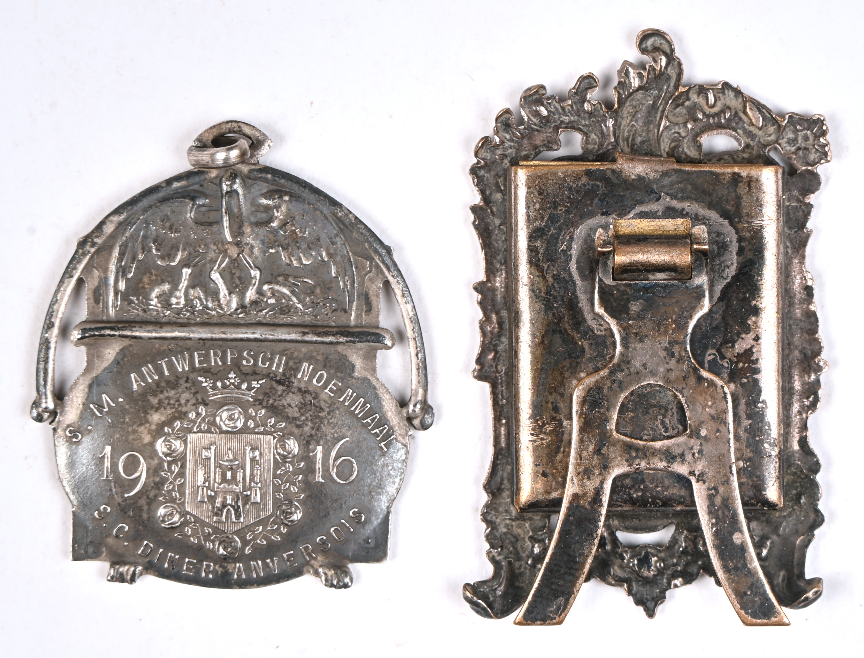 Een penning (S.M. Antwerps noenmaal 1916) en een klein verzilverd religieus object Een penning (S.M. Antwerps noenmaal 1916) en een klein verzilverd religieus object.