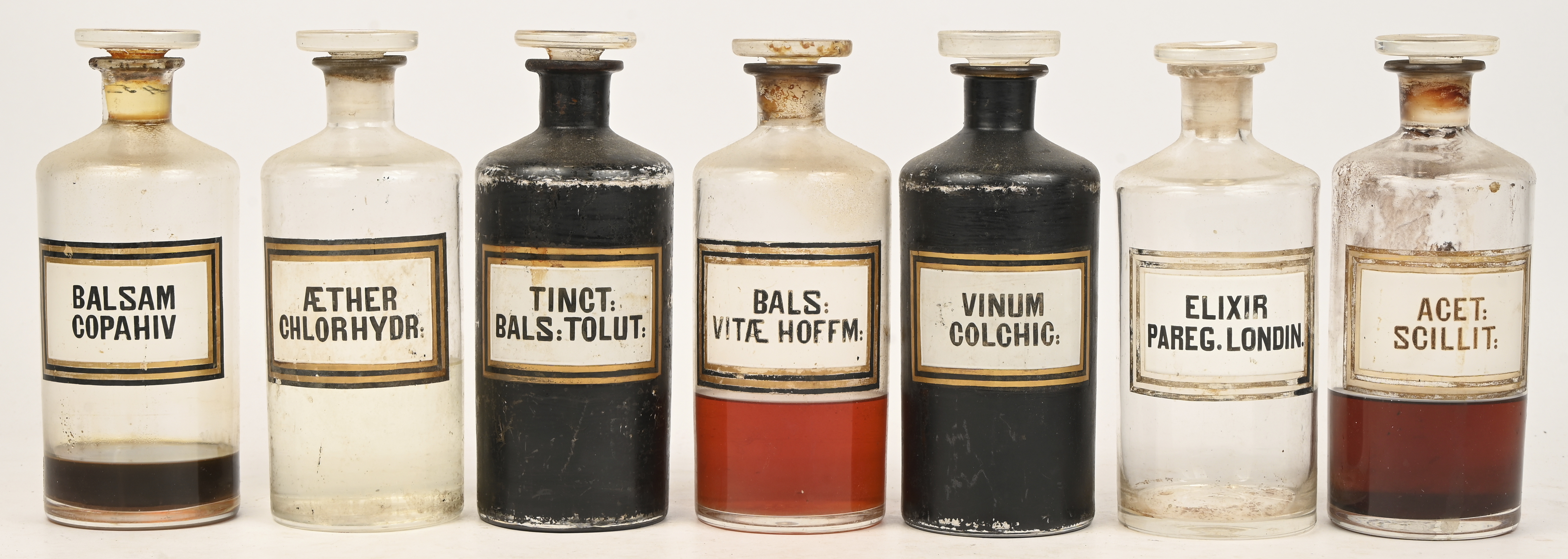 Zeven apothekersflessen met smalle hals, van kleurloos glas. Vier met inhoud, twee flessen zijn zwart geverfd Zeven apothekersflessen met smalle hals, van kleurloos glas. Vier met inhoud, twee flessen zijn zwart geverfd.