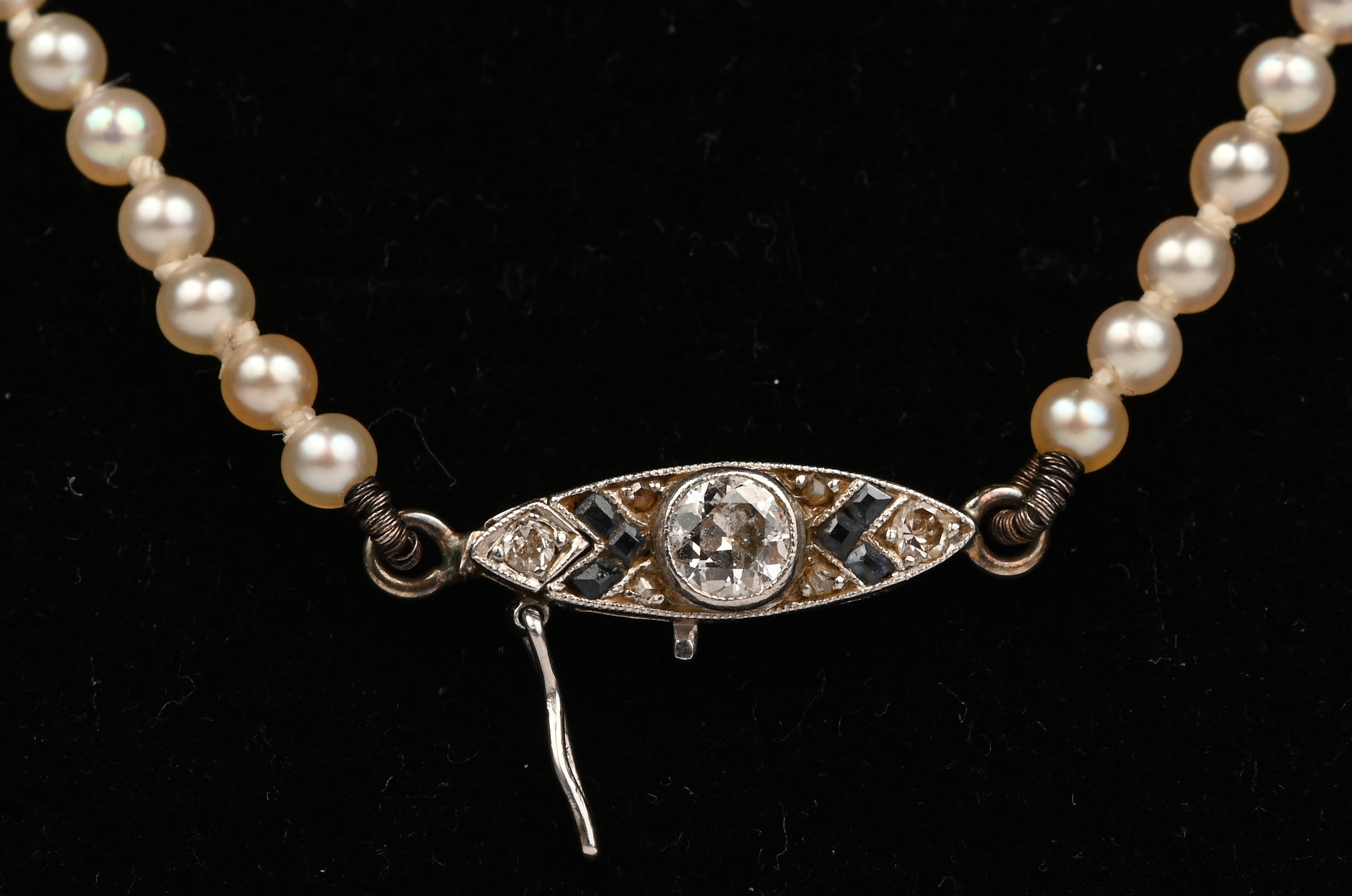 Een fijne parelhalssnoer met 18 kt witgouden slot bezet met diamanten en saffieren met een gezamenlijk gewicht van +- 0,30 ct. en een veiligheidsslot Een fijne parelhalssnoer met 18 kt witgouden slot bezet met diamanten en saffieren met een gezamenlijk gewicht van +- 0,30 ct. en een veiligheidsslot.