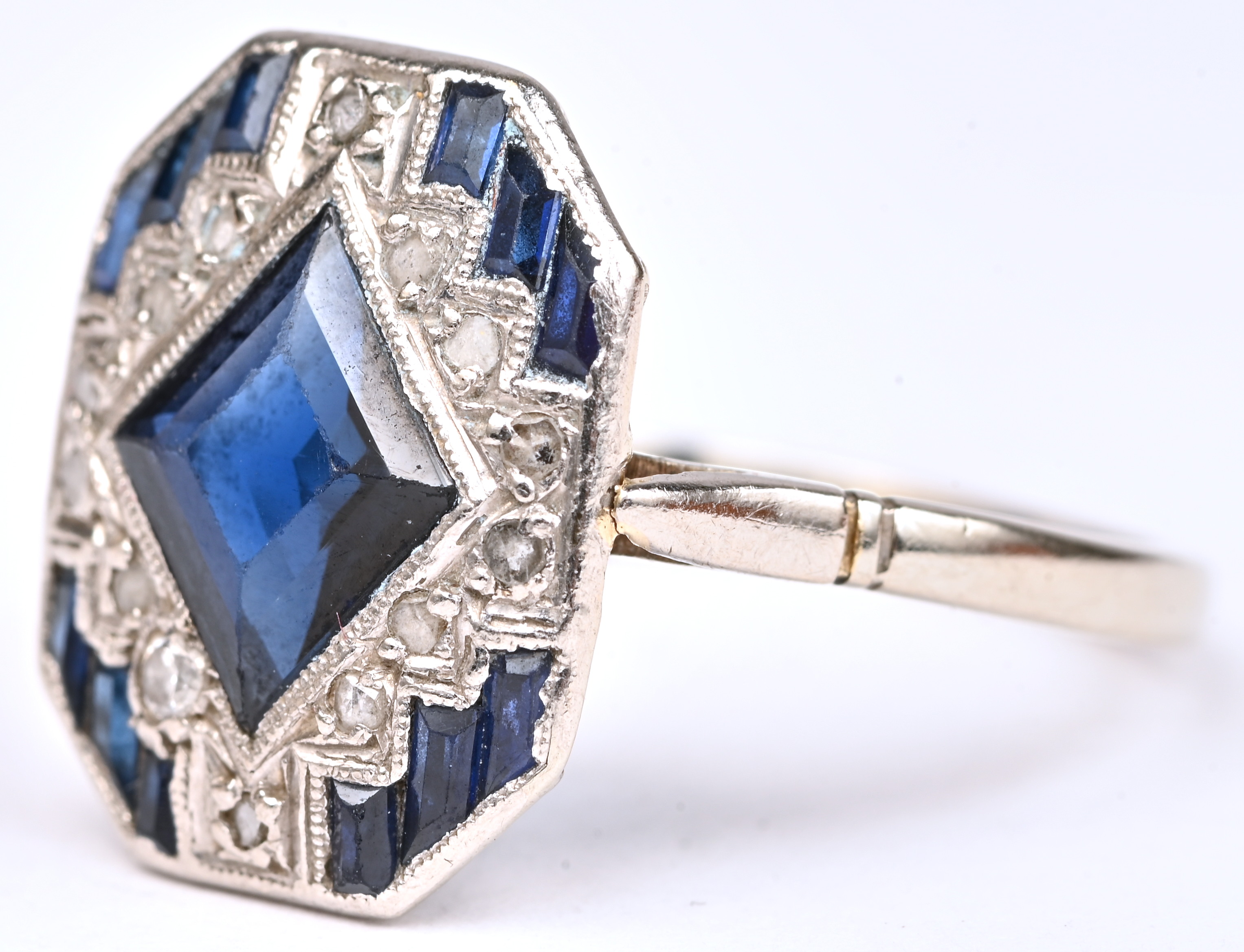 Een 18 kt witgouden art deco ring bezet met diamanten oude slijp met een gezamenlijk gewicht van +- 0,15 ct. en saffieren met een gezamenlijk gewicht van +- 1 ct Een 18 kt witgouden art deco ring bezet met diamanten oude slijp met een gezamenlijk gewicht van +- 0,15 ct. en saffieren met een gezamenlijk gewicht van +- 1 ct.