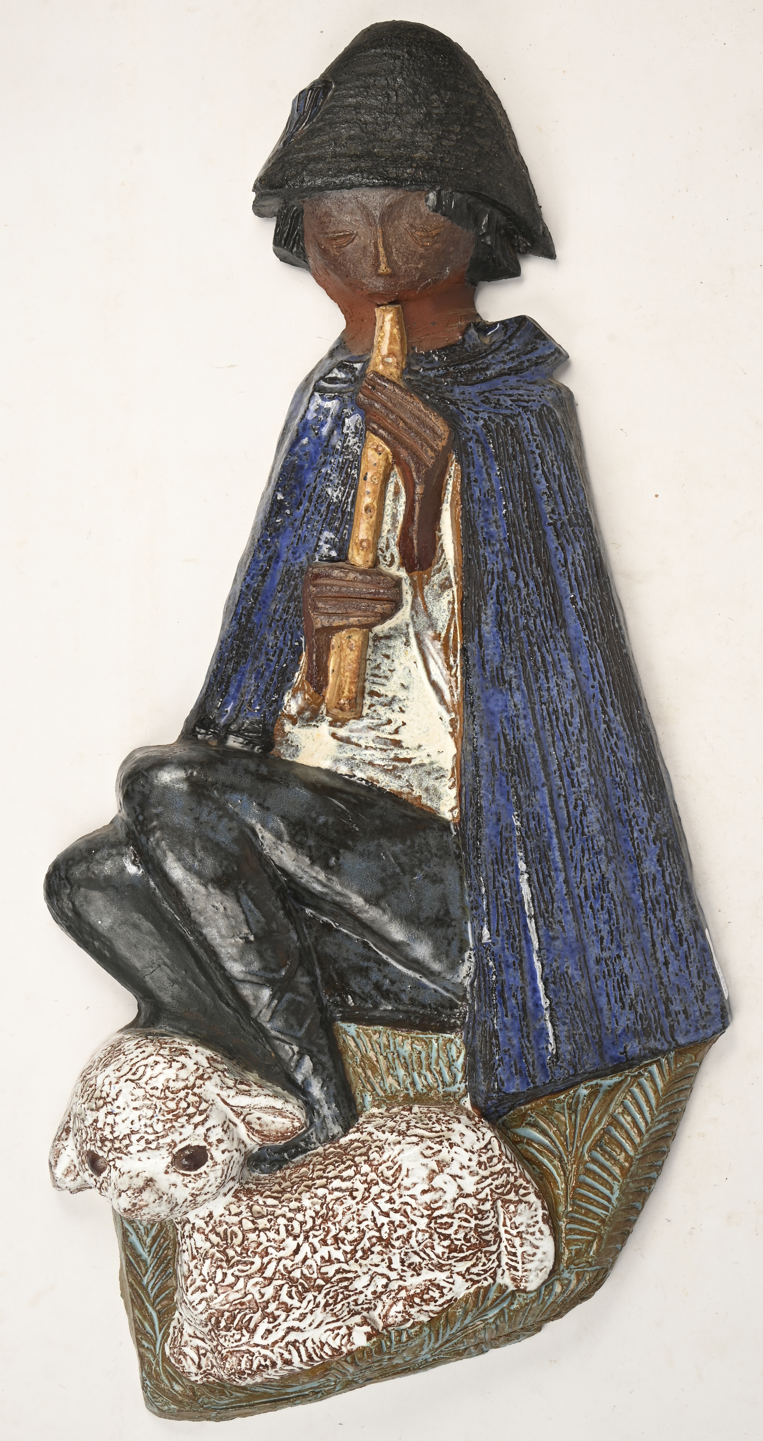 Een vintage keramische wandsculptuur voorstellend een fluitspelende herder met lammetje Een vintage keramische wandsculptuur voorstellend een fluitspelende herder met lammetje.