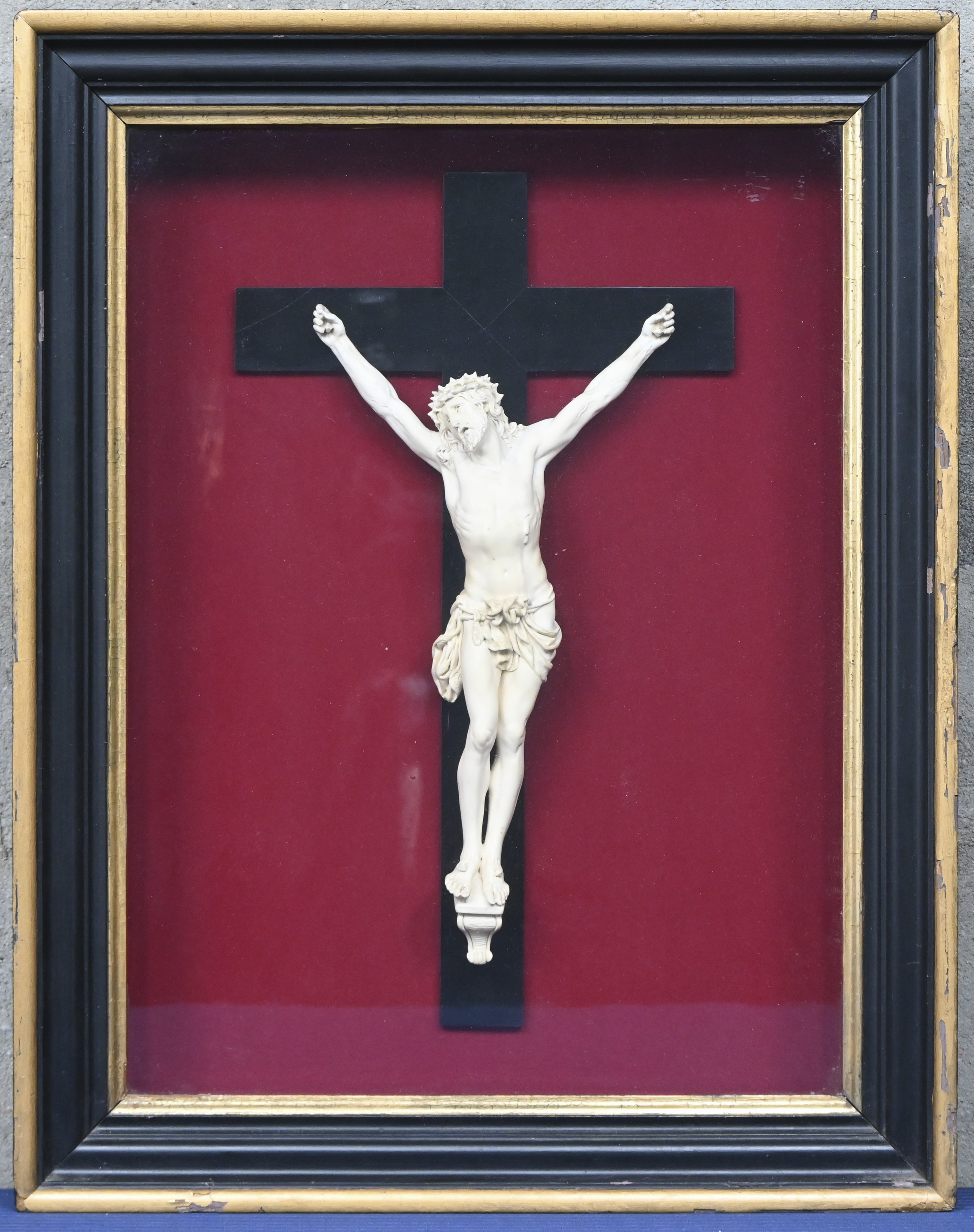 Een kruisbeeld, eerste helft 20ste eeuw, keramische Christus aan houten kruis in kader met rode vilt Een kruisbeeld, eerste helft 20ste eeuw, keramische Christus aan houten kruis in kader met rode vilt.