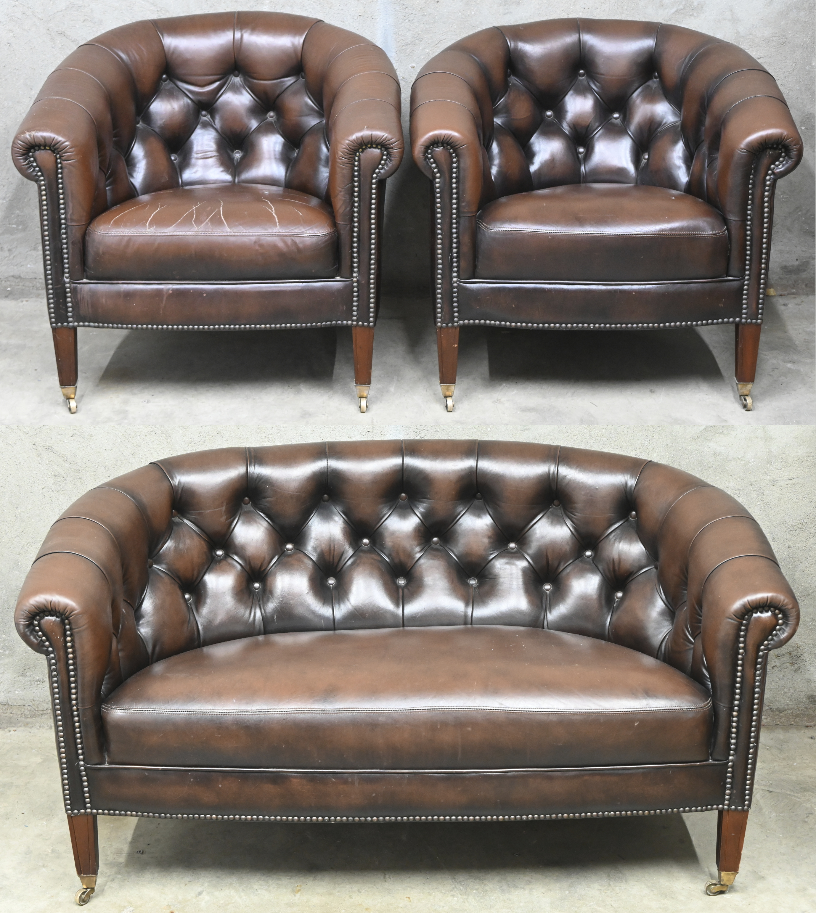 Een bruin lederen Chesterfield salonnetje op wieltjes bestaande uit een tweezit en twee clubzetels. Gebruikssporen en barsten in leer van één zetel Een bruin lederen Chesterfield salonnetje op wieltjes bestaande uit een tweezit en twee clubzetels. Gebruikssporen en barsten in leer van één zetel.