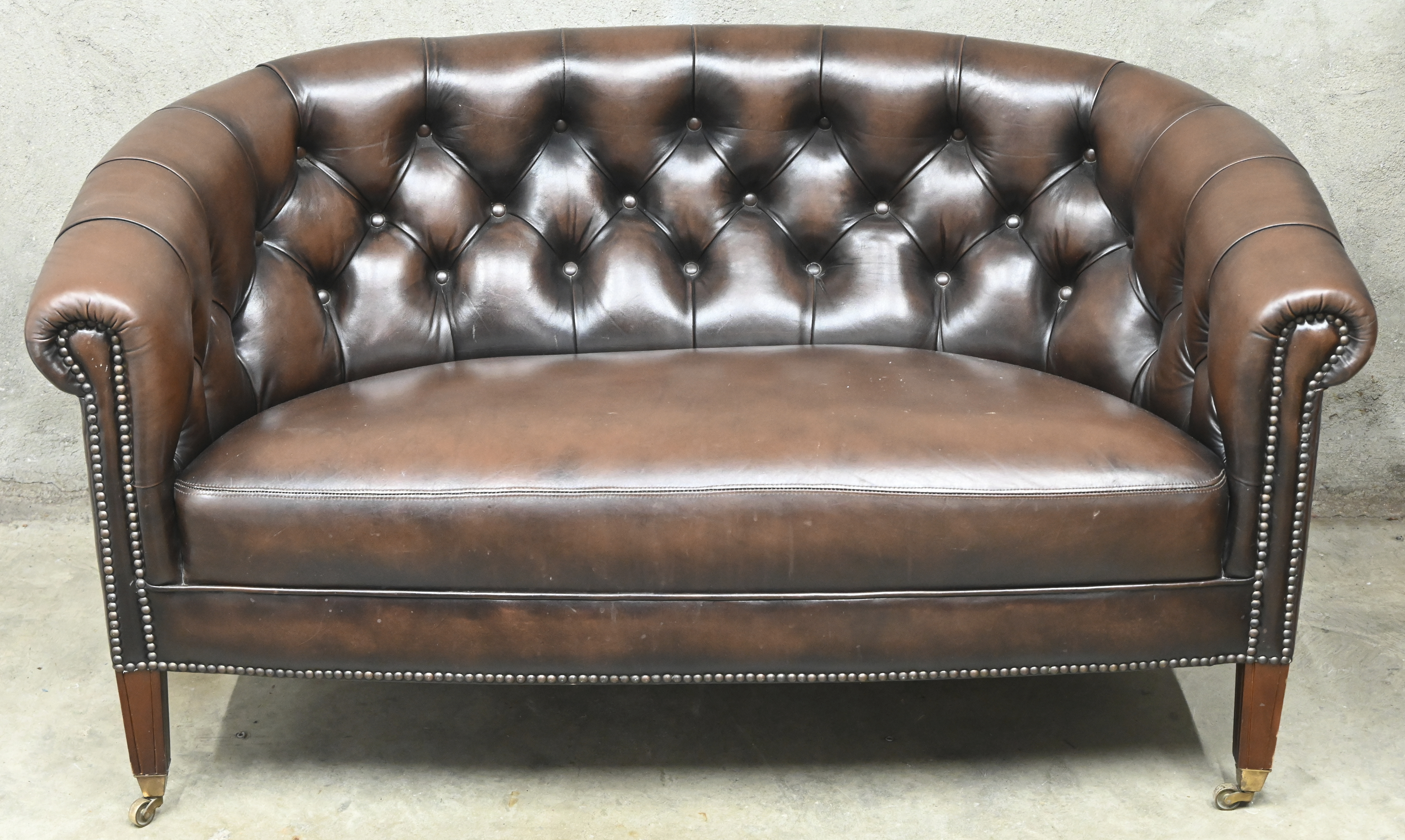 Een bruin lederen Chesterfield salonnetje op wieltjes bestaande uit een tweezit en twee clubzetels. Gebruikssporen en barsten in leer van één zetel Een bruin lederen Chesterfield salonnetje op wieltjes bestaande uit een tweezit en twee clubzetels. Gebruikssporen en barsten in leer van één zetel.