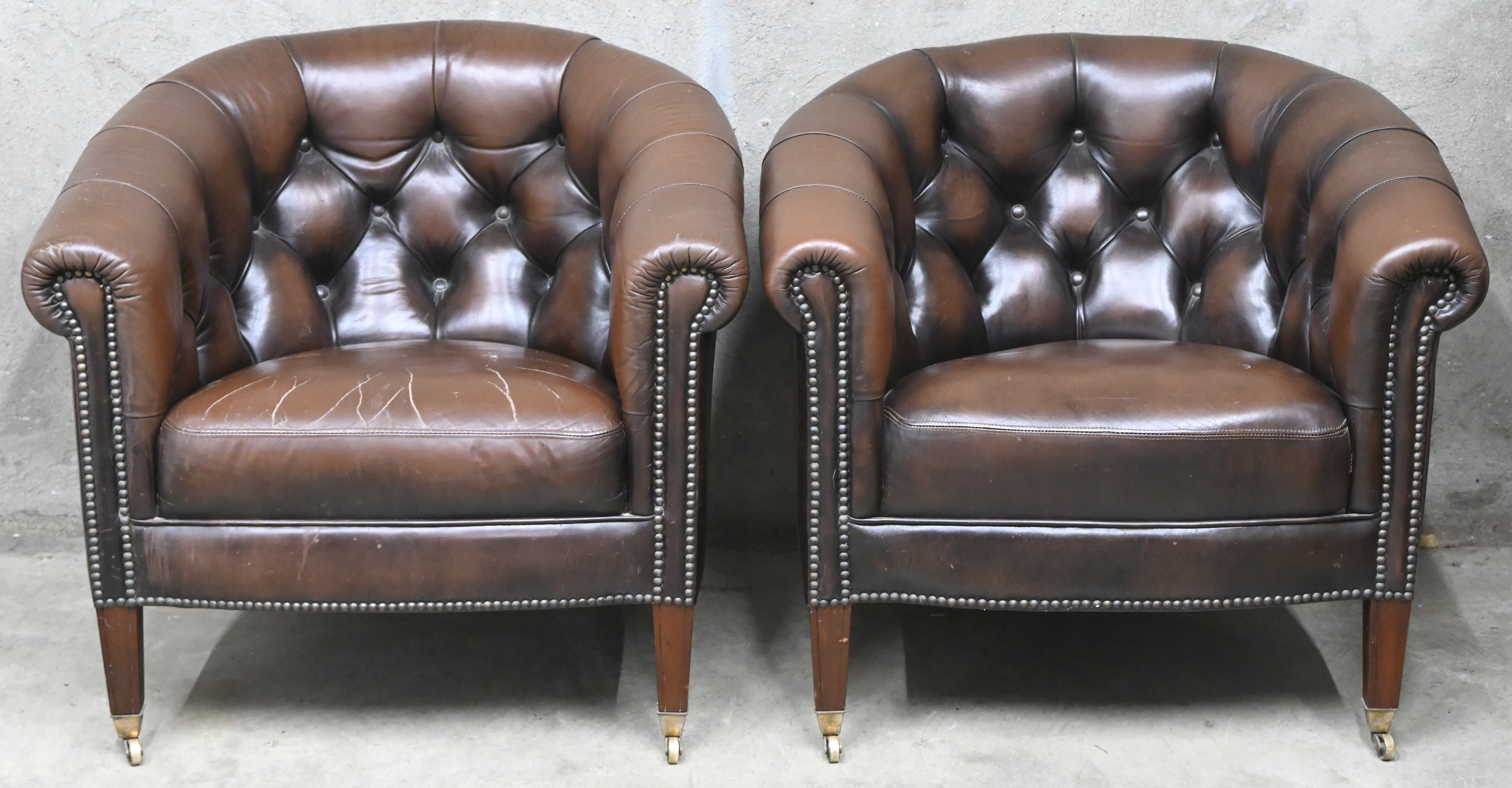 Een bruin lederen Chesterfield salonnetje op wieltjes bestaande uit een tweezit en twee clubzetels. Gebruikssporen en barsten in leer van één zetel Een bruin lederen Chesterfield salonnetje op wieltjes bestaande uit een tweezit en twee clubzetels. Gebruikssporen en barsten in leer van één zetel.