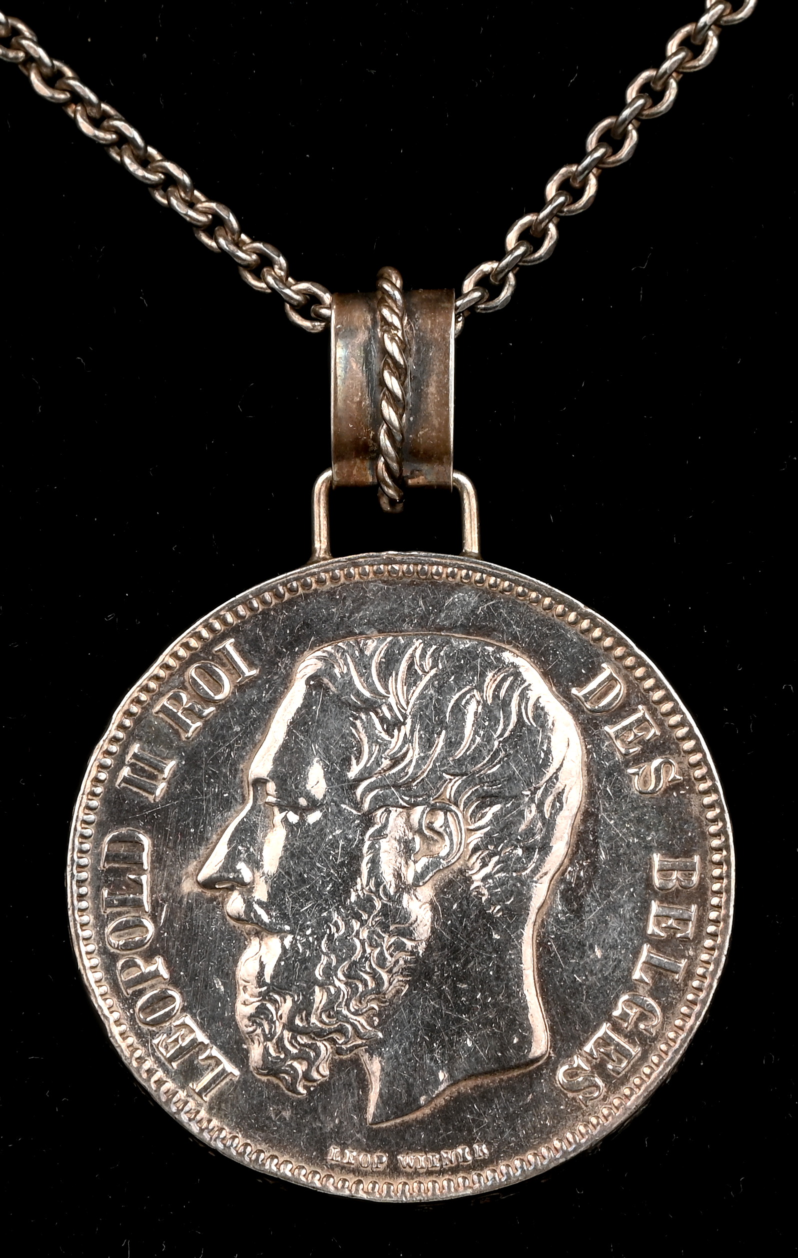 Een ketting met een hanger van zilver met een 5 Franc munt van Leopold II en wapenschild. 1870 Een ketting met een hanger van zilver met een 5 Franc munt van Leopold II en wapenschild. 1870.