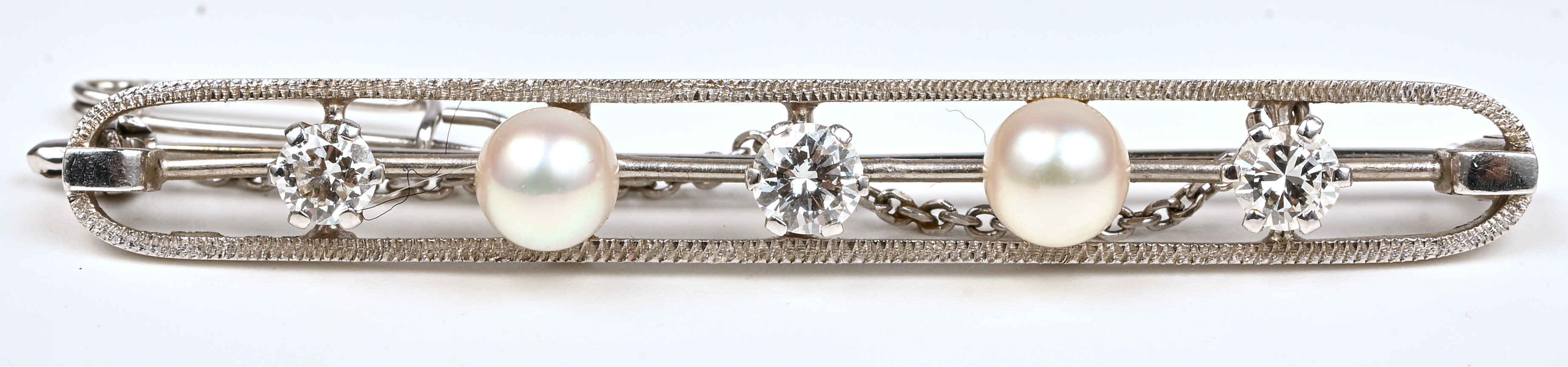 Een 18 kt witgouden broche bezet met drie briljanten met een gezamenlijk gewicht van +- 0,60 ct. en twee parels Een 18 kt witgouden broche bezet met drie briljanten met een gezamenlijk gewicht van +- 0,60 ct. en twee parels.