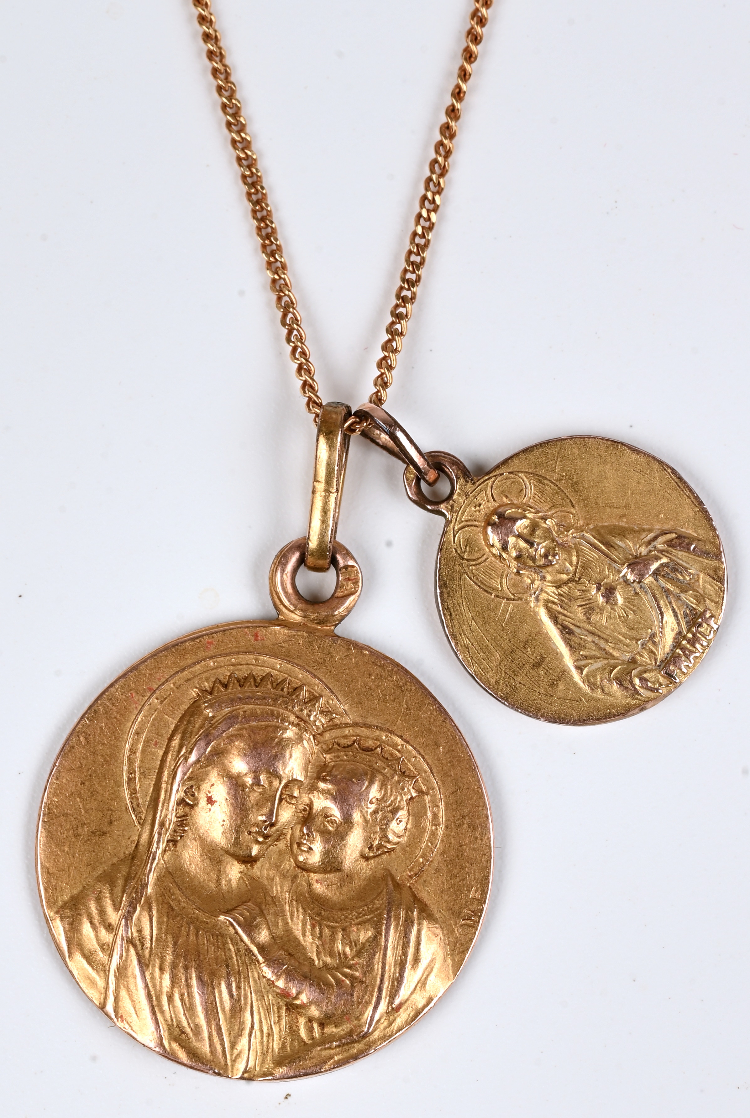 Een 18 kt geelgouden ketting met twee hangers met de voorstelling van Modonna en kind en een Heilige voordtelling en Heilig Hart. Gemerkt France. M.F. 1921 Een 18 kt geelgouden ketting met twee hangers met de voorstelling van Modonna en kind en een Heilige voordtelling en Heilig Hart. Gemerkt France. M.F. 1921.