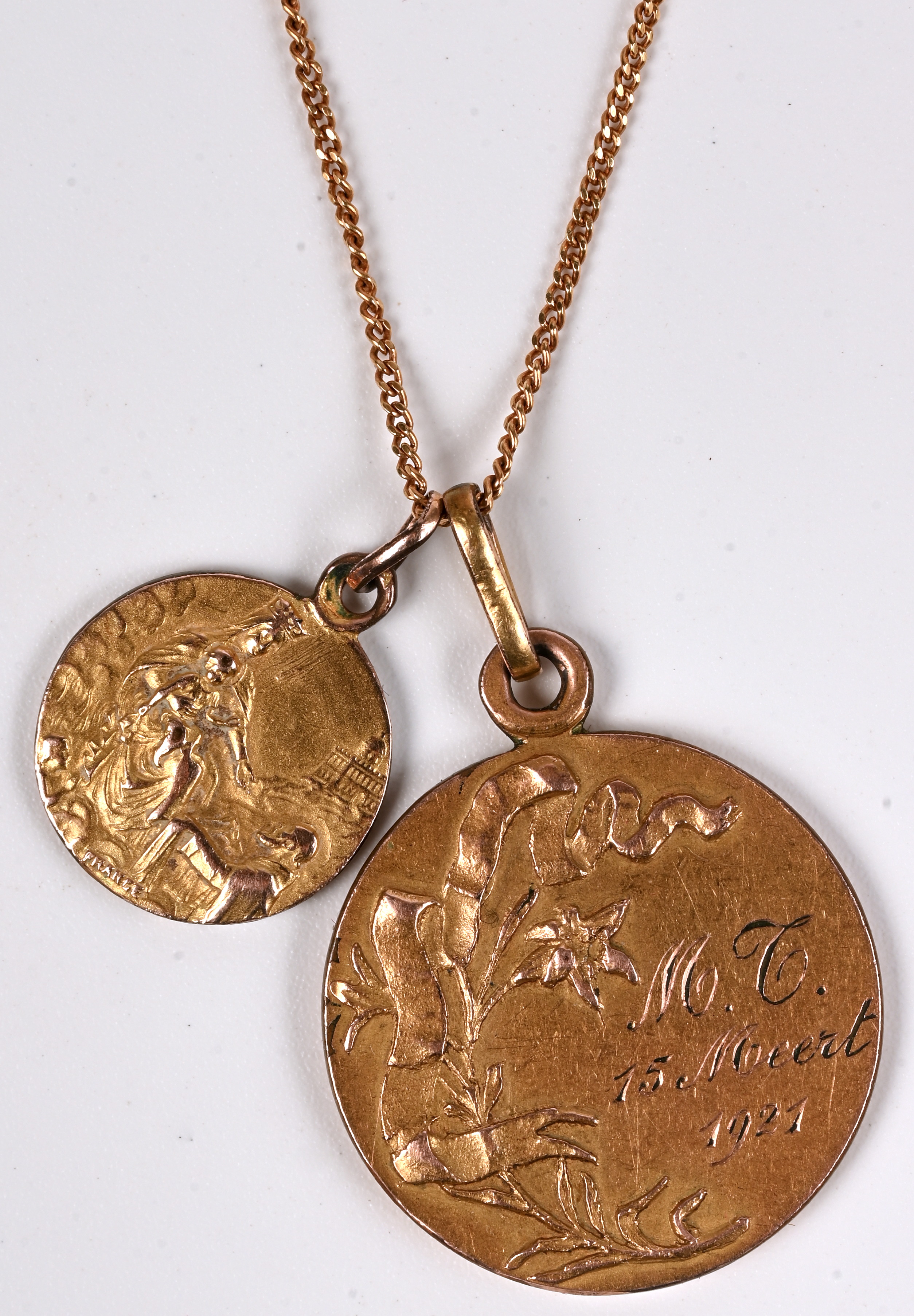 Een 18 kt geelgouden ketting met twee hangers met de voorstelling van Modonna en kind en een Heilige voordtelling en Heilig Hart. Gemerkt France. M.F. 1921 Een 18 kt geelgouden ketting met twee hangers met de voorstelling van Modonna en kind en een Heilige voordtelling en Heilig Hart. Gemerkt France. M.F. 1921.