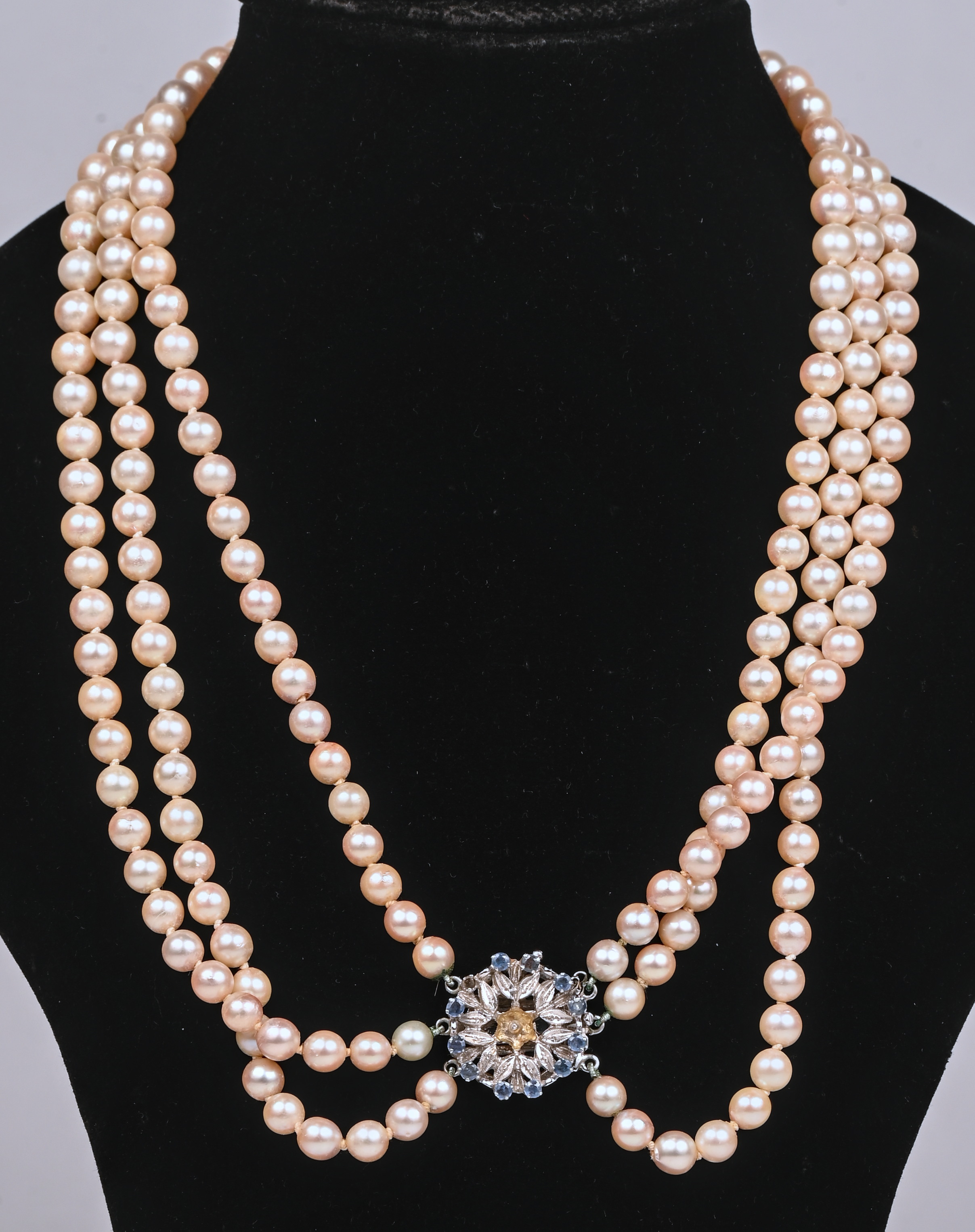 Een drie rijen parelhalssnoer met 18 witgouden slot bezet met saffier. (twee steentjes ontbreken) Een drie rijen parelhalssnoer met 18 witgouden slot bezet met saffier. (twee steentjes ontbreken).