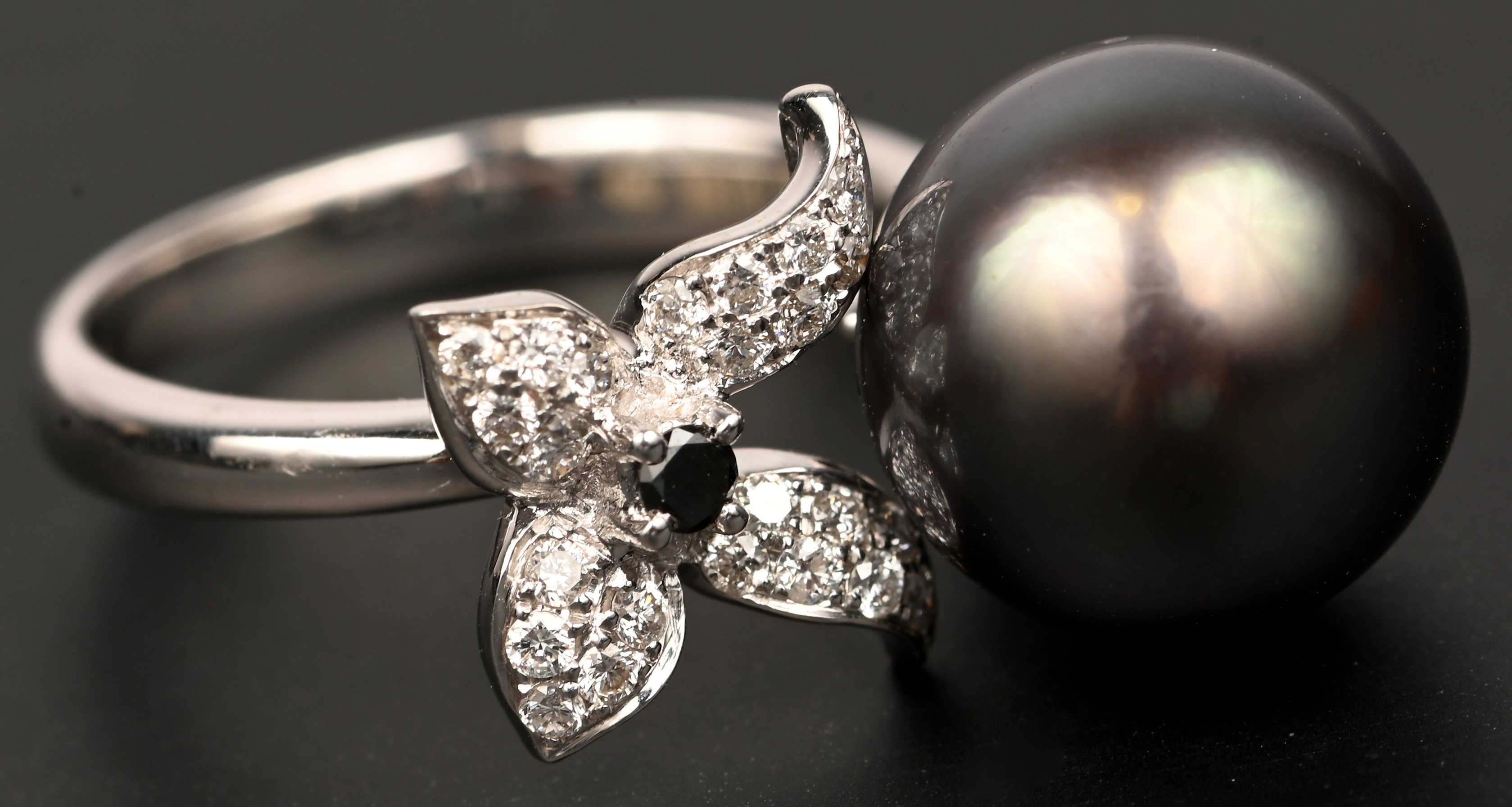 Een 18 karaats witgouden ring met met centrale parel en 1 zwart briljantje en witte briljanten met een gezamenlijk gewicht van +- 0,30 ct Een 18 karaats witgouden ring met met centrale parel en 1 zwart briljantje en witte briljanten met een gezamenlijk gewicht van +- 0,30 ct.