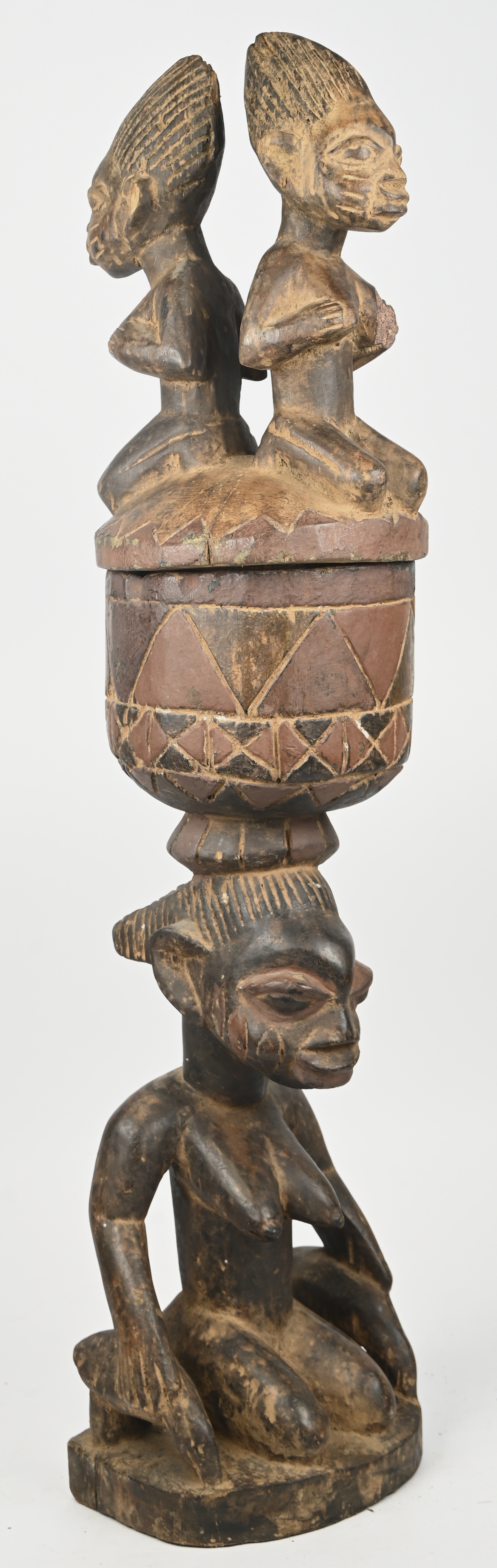 Een houten recipiënt met deksel, gedragen door een knielende vrouw. Op het deksel twee kleine knielende vrouwen. Joruba, Benin Een houten recipiënt met deksel, gedragen door een knielende vrouw. Op het deksel twee kleine knielende vrouwen. Joruba, Benin.